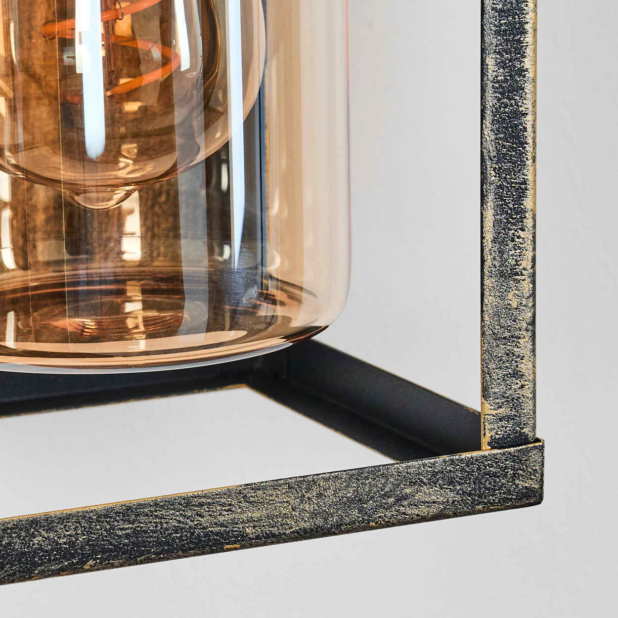 Nahaufnahme einer Lampe. Sie hat ein klares Glas mit einer Glühbirne im Inneren, eingefasst in einen schwarz-goldenen Metallrahmen.