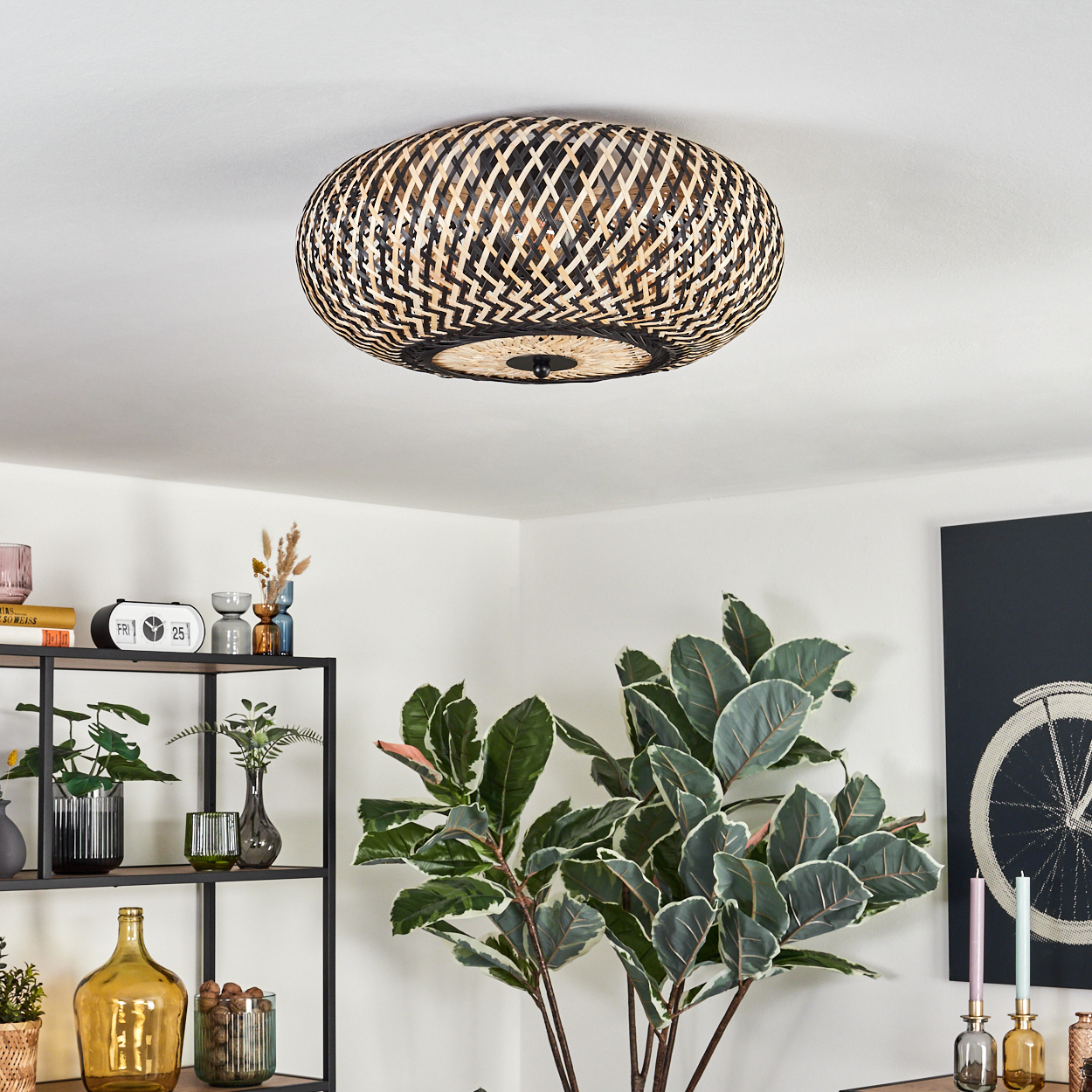 Eine gewebte Lampe hängt von der Decke. Darunter befindet sich ein Regal mit Dekoration und Pflanzen. Rechts ist eine große Pflanze.