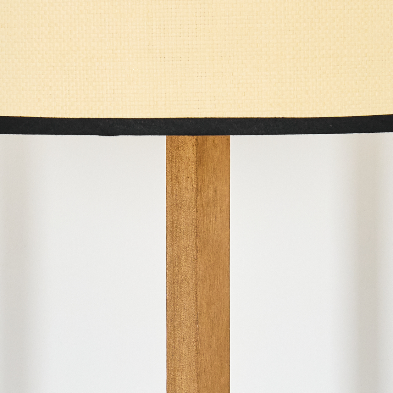 Nahaufnahme einer Lampe. Der Lampenschirm ist beige mit schwarzem Rand. Die Holzstütze der Lampe ist vor weißem Hintergrund sichtbar.