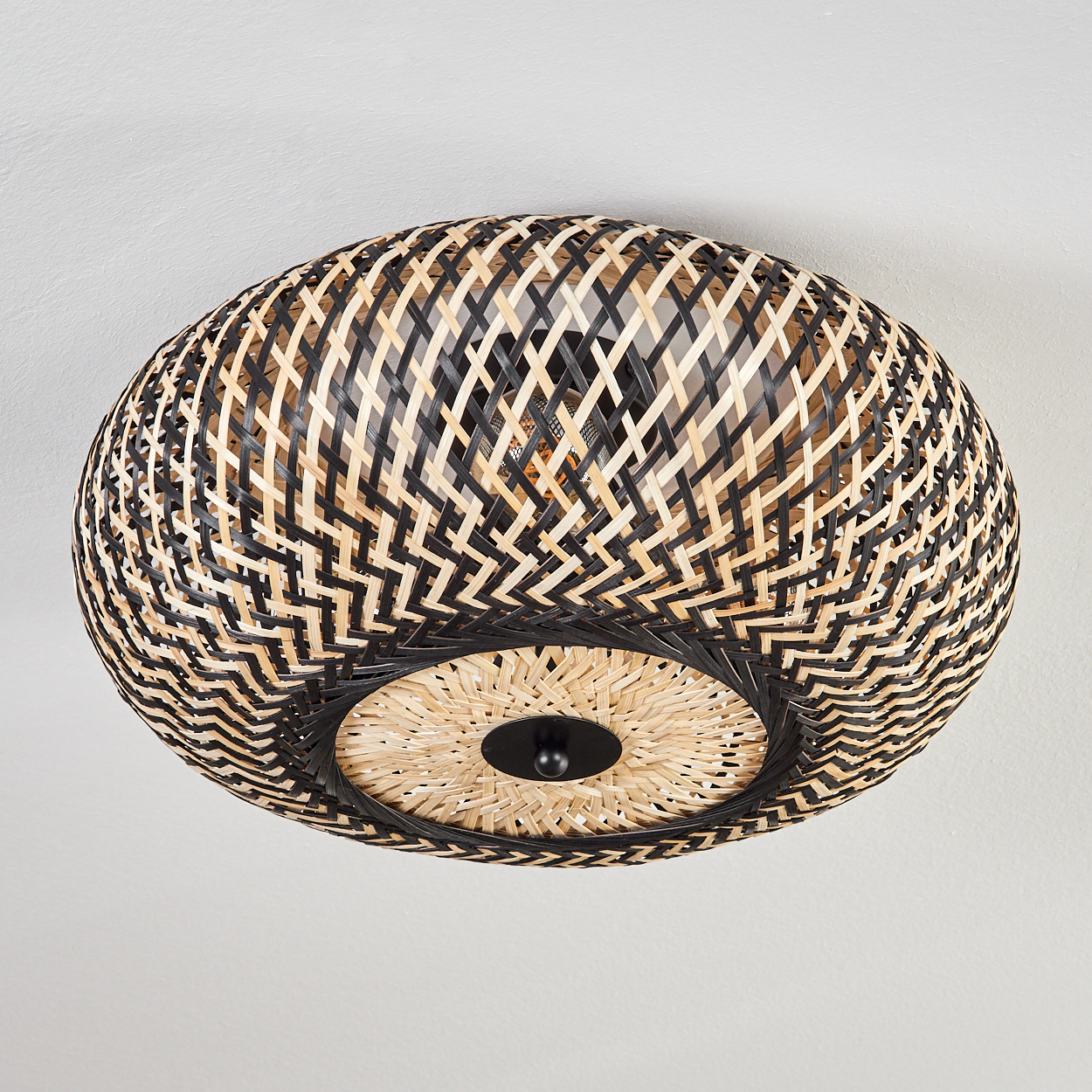 Eine Deckenlampe aus geflochtenem Rattan mit schwarzen und natürlichen Webmustern, kreisförmig, mit schwarzer Scheibe.