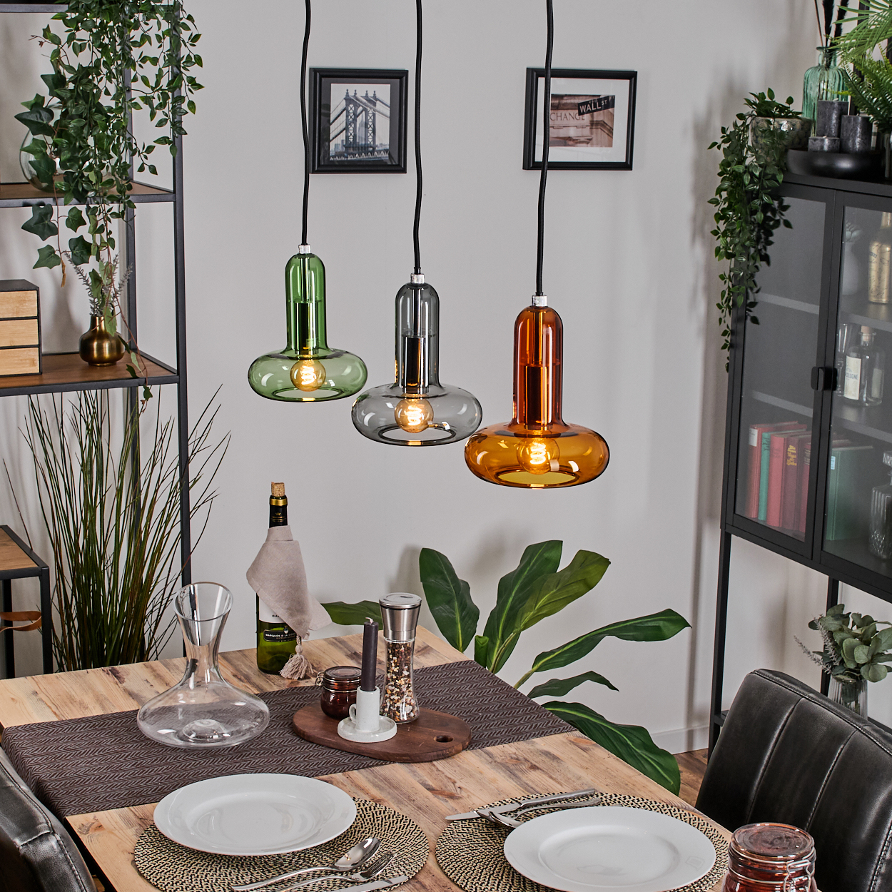 Esszimmer mit Holztisch, drei bunten Hängelampen und einem schwarzen Schrank. Tisch für zwei Personen mit Tellern und Besteck gedeckt.