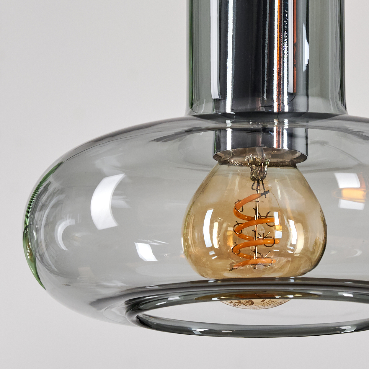 Nahaufnahme einer stilvollen Leuchte. Sie hat einen klaren Glasschirm mit einer warm leuchtenden Glühbirne. Die Leuchte hat einen Metallaufsatz.