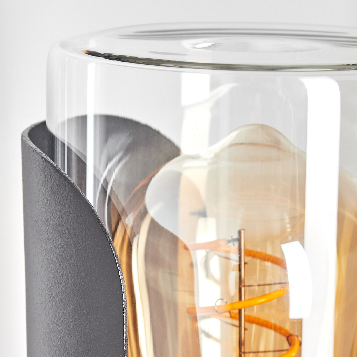 Nahaufnahme einer Glühbirne in einem Glaszylinder, umschlossen von einem dunklen Metallrahmen, vor weißem Hintergrund.