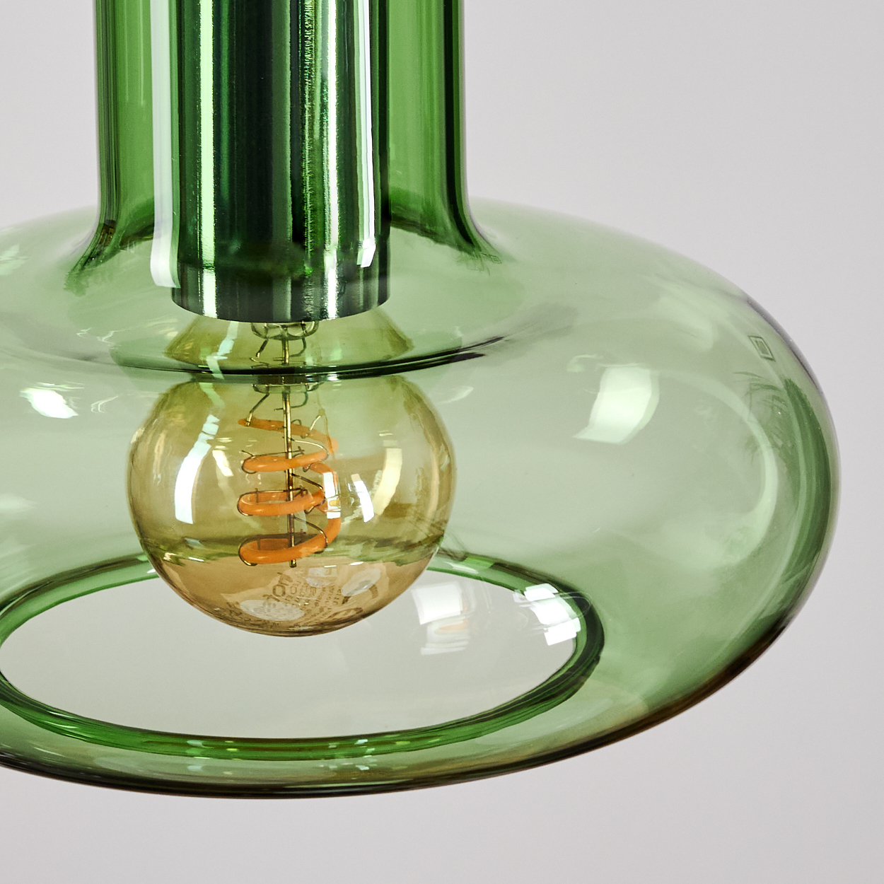 Eine grüne Glas-Pendelleuchte mit einer Glühbirne. Die Glühbirne hat einen Wendelfaden. Der Hintergrund ist schlicht weiß.