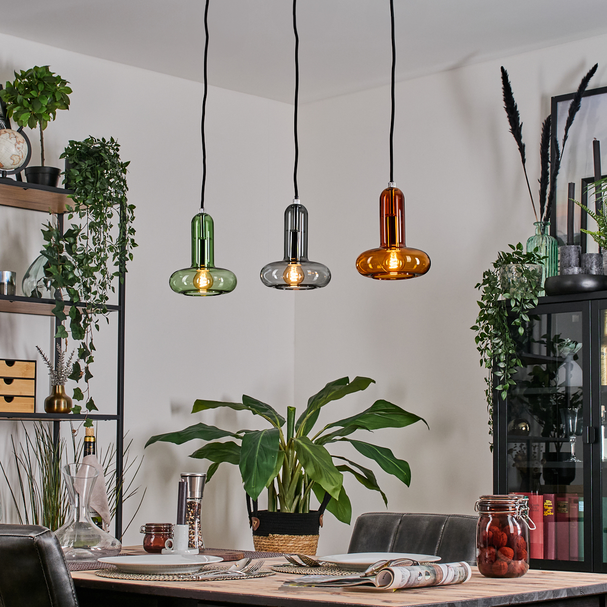 Esszimmer mit drei farbigen Pendelleuchten. Tisch mit Tellern gedeckt. Pflanzen im Hintergrund.