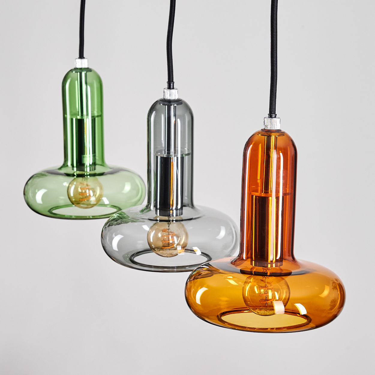 Drei bunte Pendelleuchten hängen. Grüne, graue und orangefarbene Glasschirme mit freiliegenden Glühbirnen.