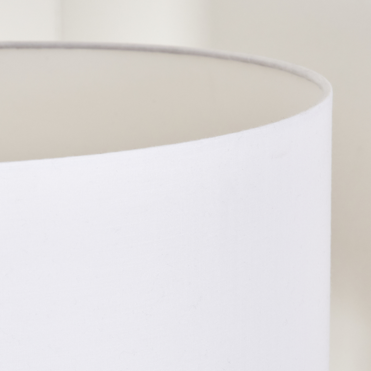 Nahaufnahme eines weißen Lampenschirms mit gebogenem oberem Rand. Der Hintergrund ist eine weiche, neutrale Farbe.
