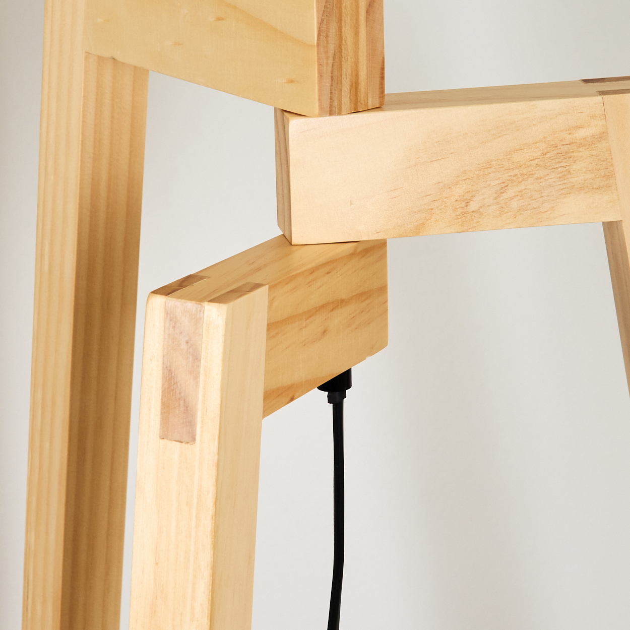 Nahaufnahme von Holzstruktur mit Verbindungen und Beinen. Ein schwarzes Kabel verläuft entlang eines Beins. Der Hintergrund ist weiß.