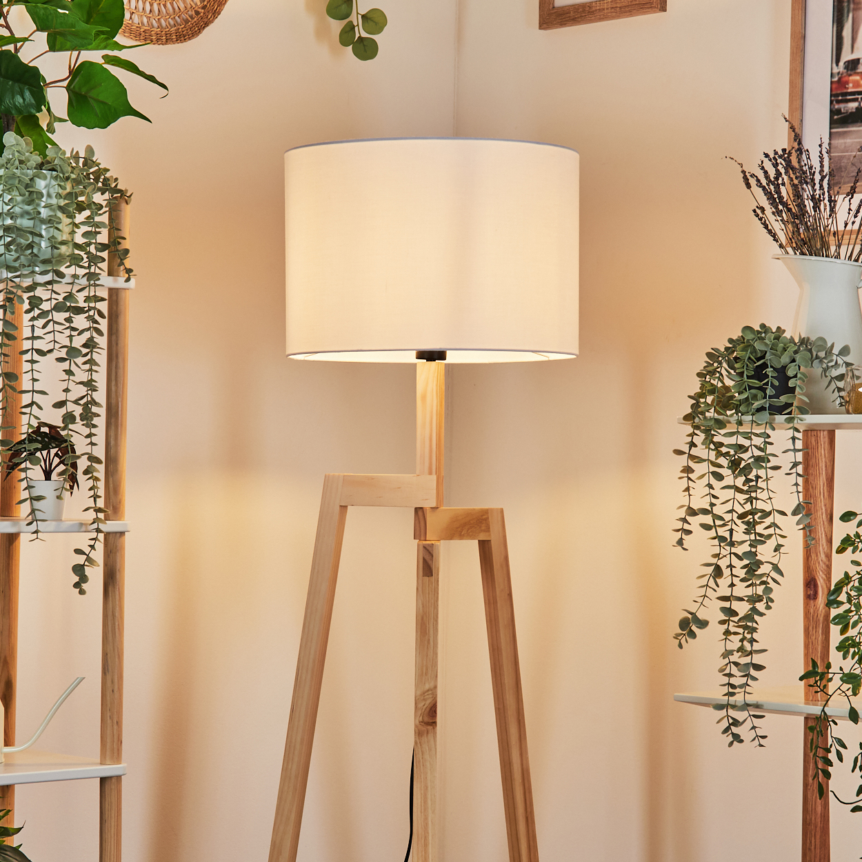 Eine Holz-Stehlampe mit weißem Lampenschirm steht in einer Ecke. Auf beiden Seiten Regale mit Pflanzen. Rechts eine Vase mit Lavendel.