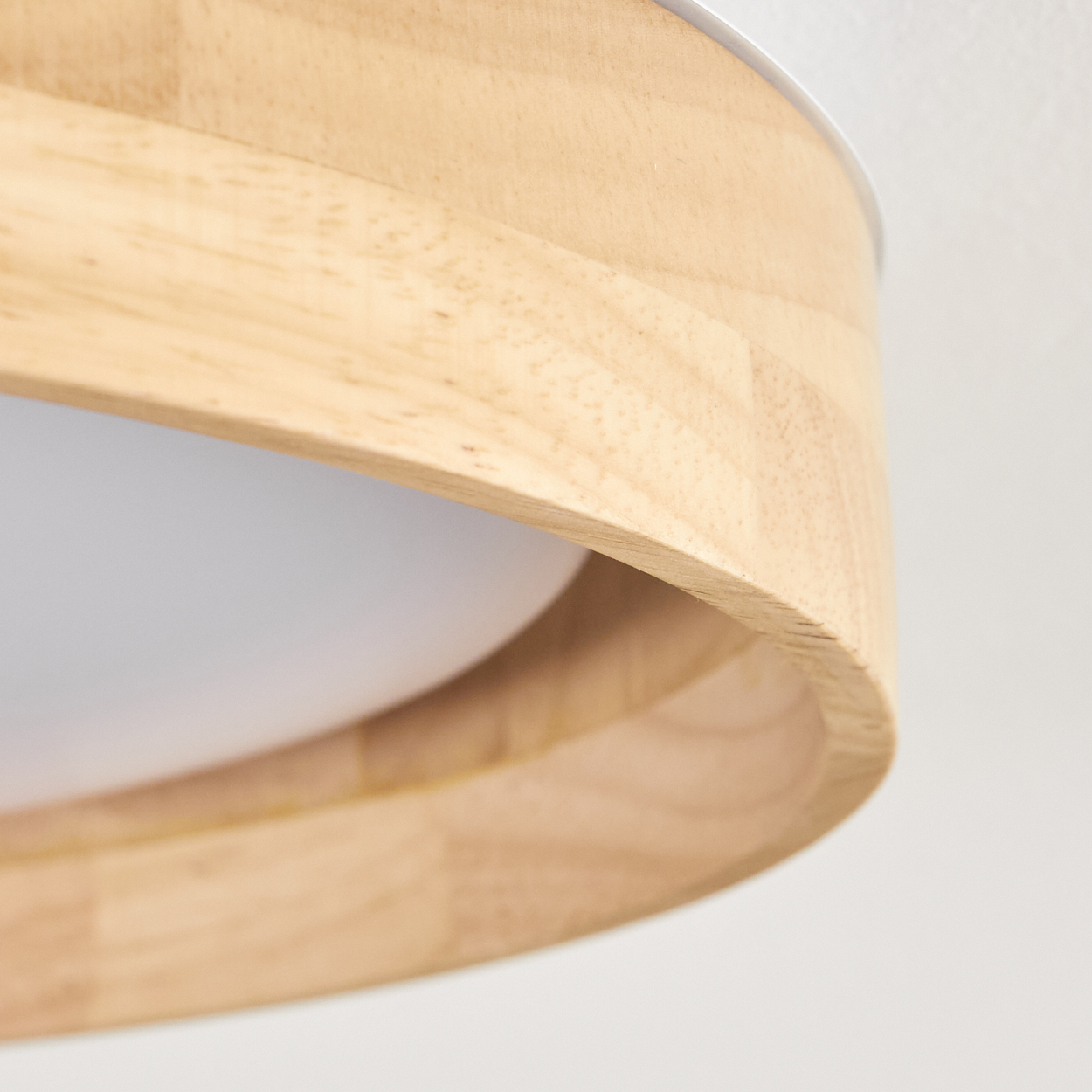 Nahaufnahme eines Holzlampenschirms mit geschwungenem Design. Der Schirm ist hellbraun, zeigt Maserung, und weißes Licht wird gestreut.
