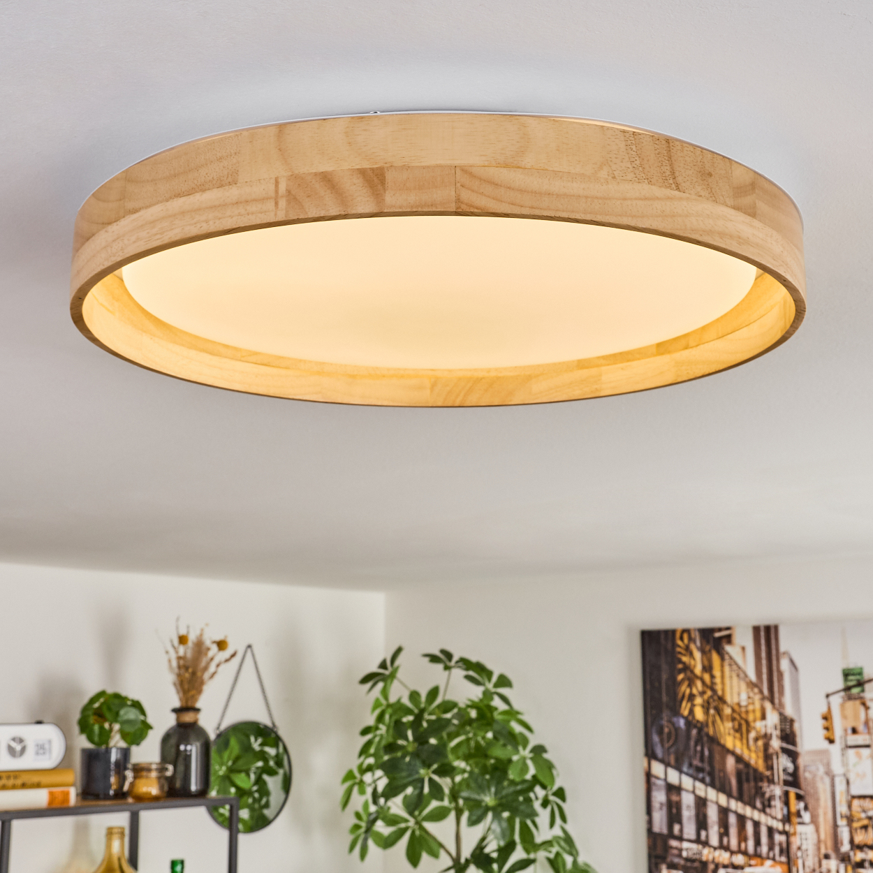 Eine runde Deckenleuchte aus Holz mit hellem Zentrum. Verschiedene Pflanzen und Dekorationen sind unten zu sehen, zusammen mit einem Stadtkunstwerk.