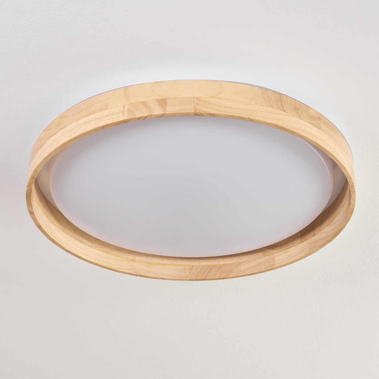 Eine kreisförmige Deckenleuchte. Sie hat einen hellen Holzrahmen um eine weiße, undurchsichtige zentrale Lichtplatte. An einer weißen Decke montiert.