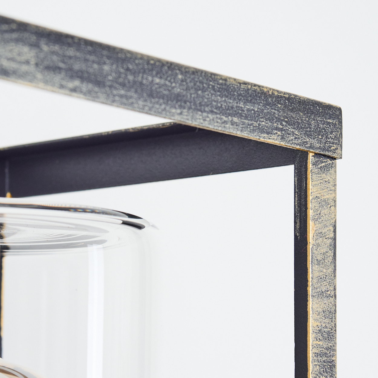 Nahaufnahme eines dekorativen Metallrahmens mit einem Glasgefäß. Der Rahmen ist schwarz und gold, mit weißem Hintergrund.
