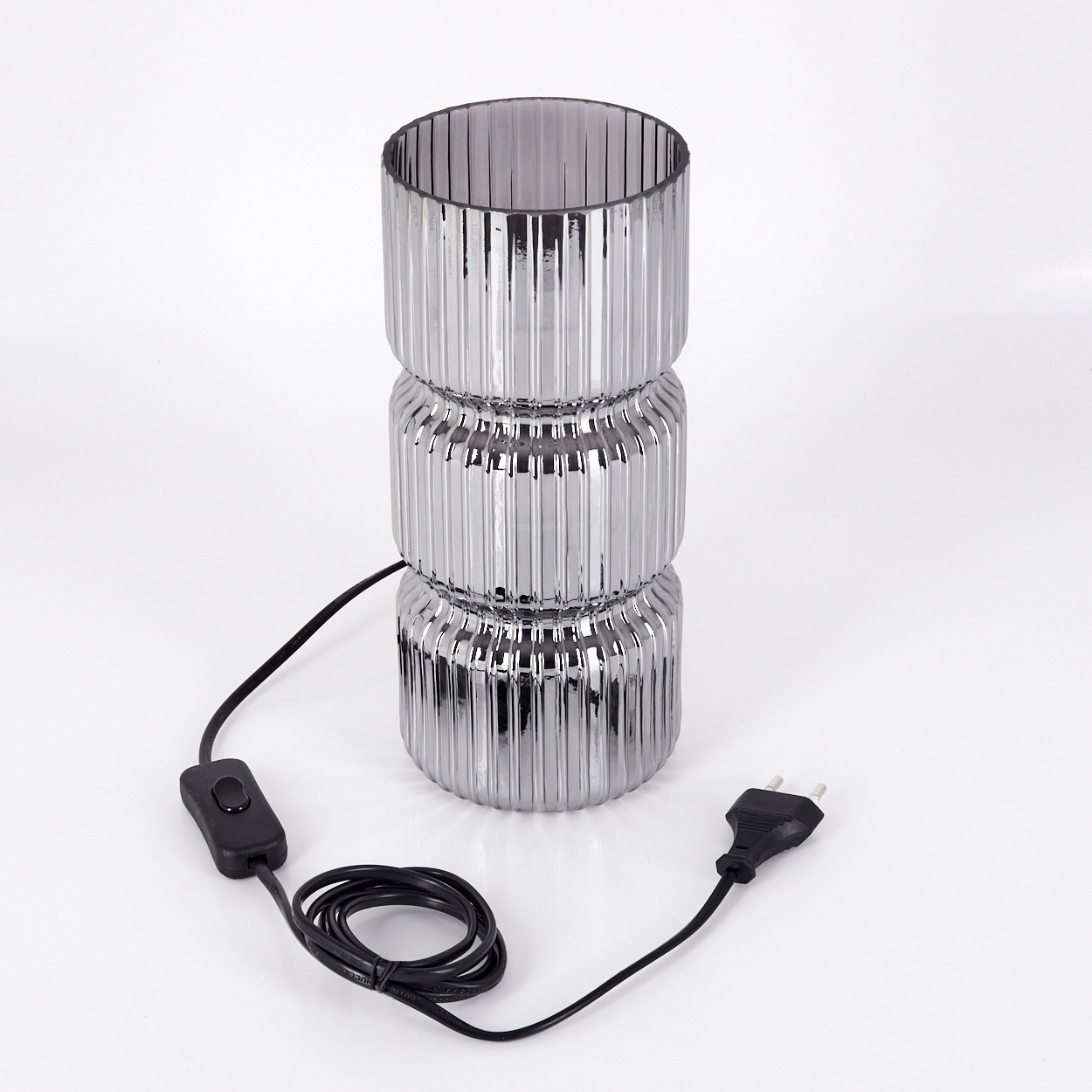Eine silberne, geriffelte Glaslampe mit schwarzem Kabel, Schalter und Stecker auf weißem Hintergrund.