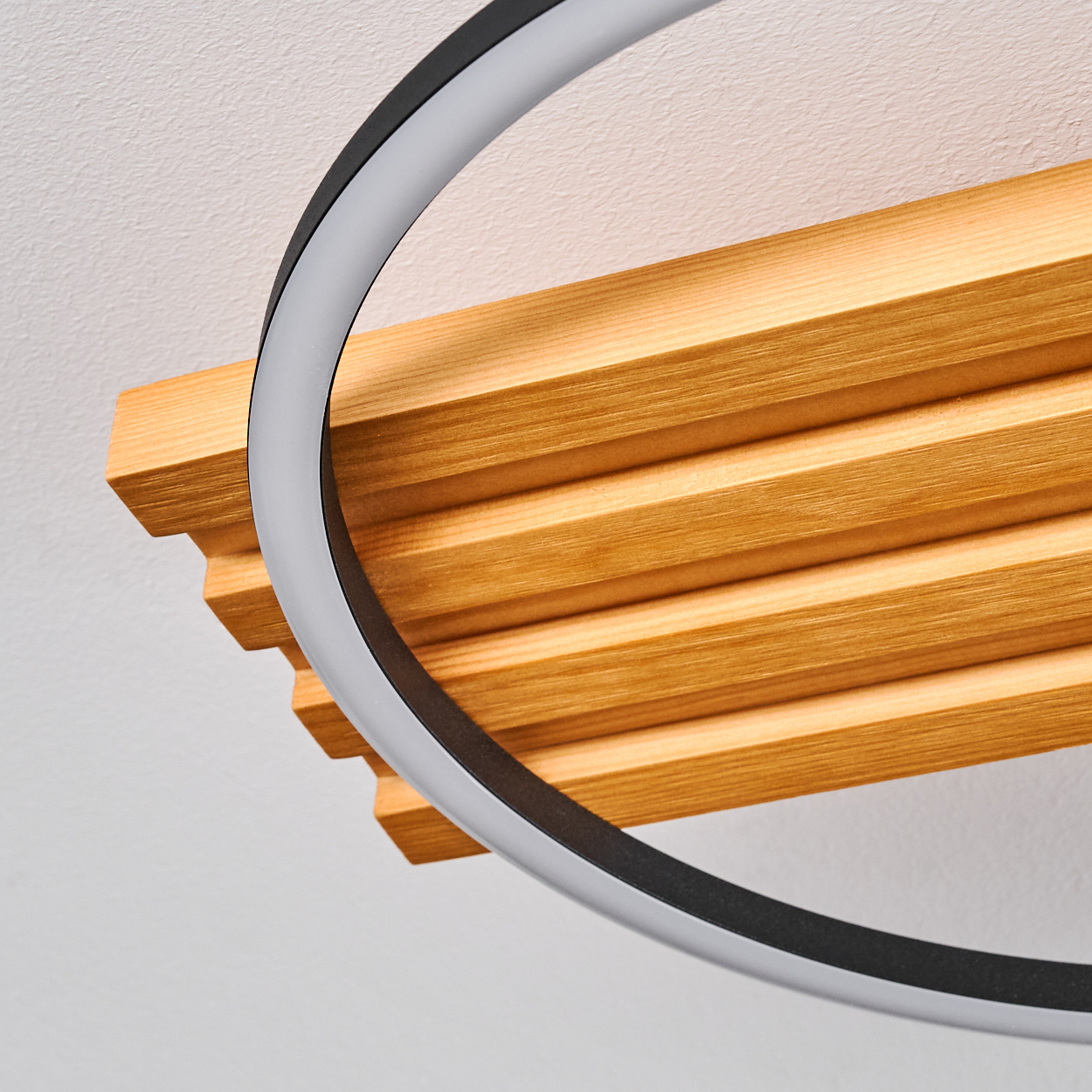 Eine moderne Leuchte mit kreisförmigem Design. Sie ist an einer Holzlatten-Decke mit weißem Hintergrund befestigt.
