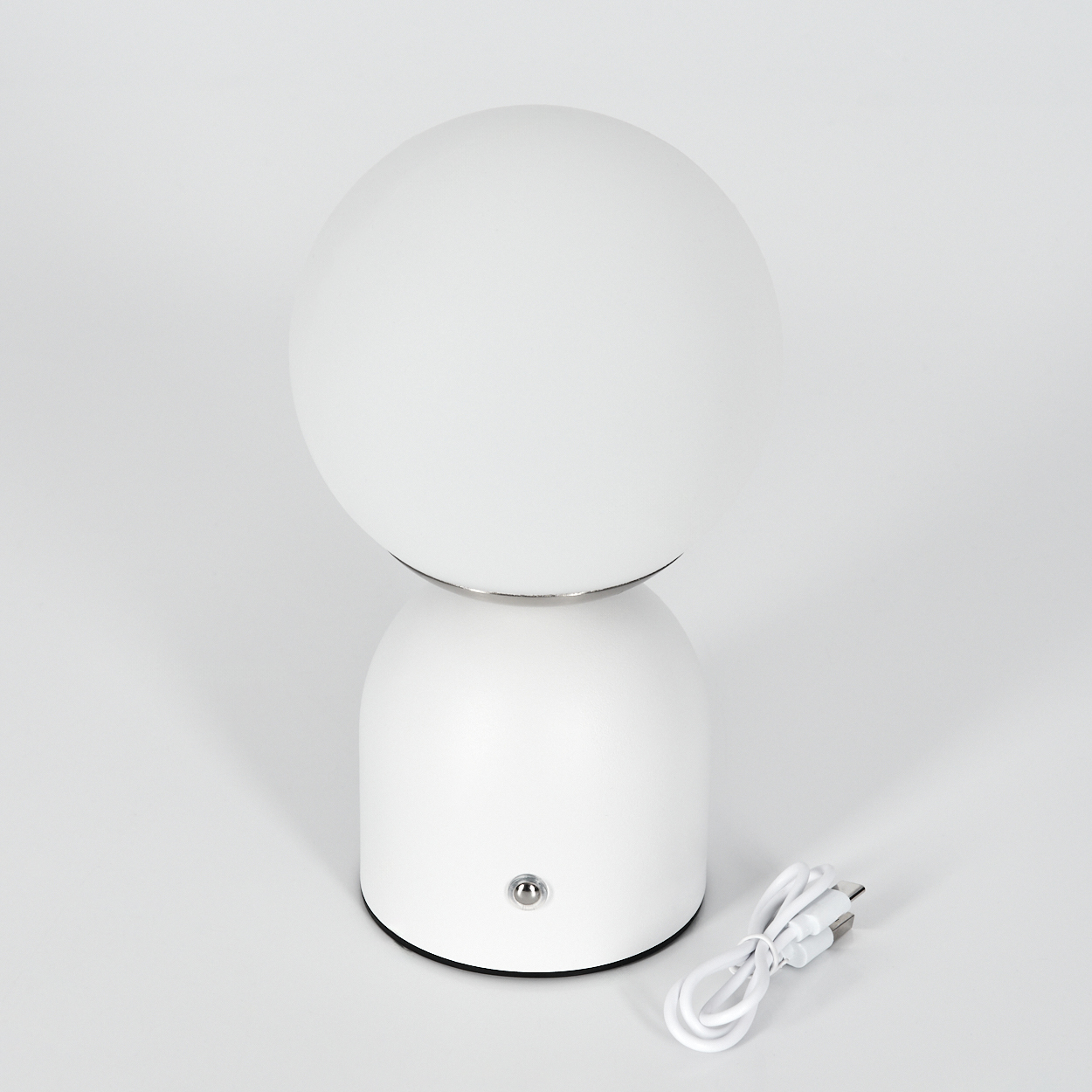 Eine weiße Tischlampe mit rundem Lampenschirm und zylindrischem Sockel. Ein weißes Kabel liegt neben der Lampe.