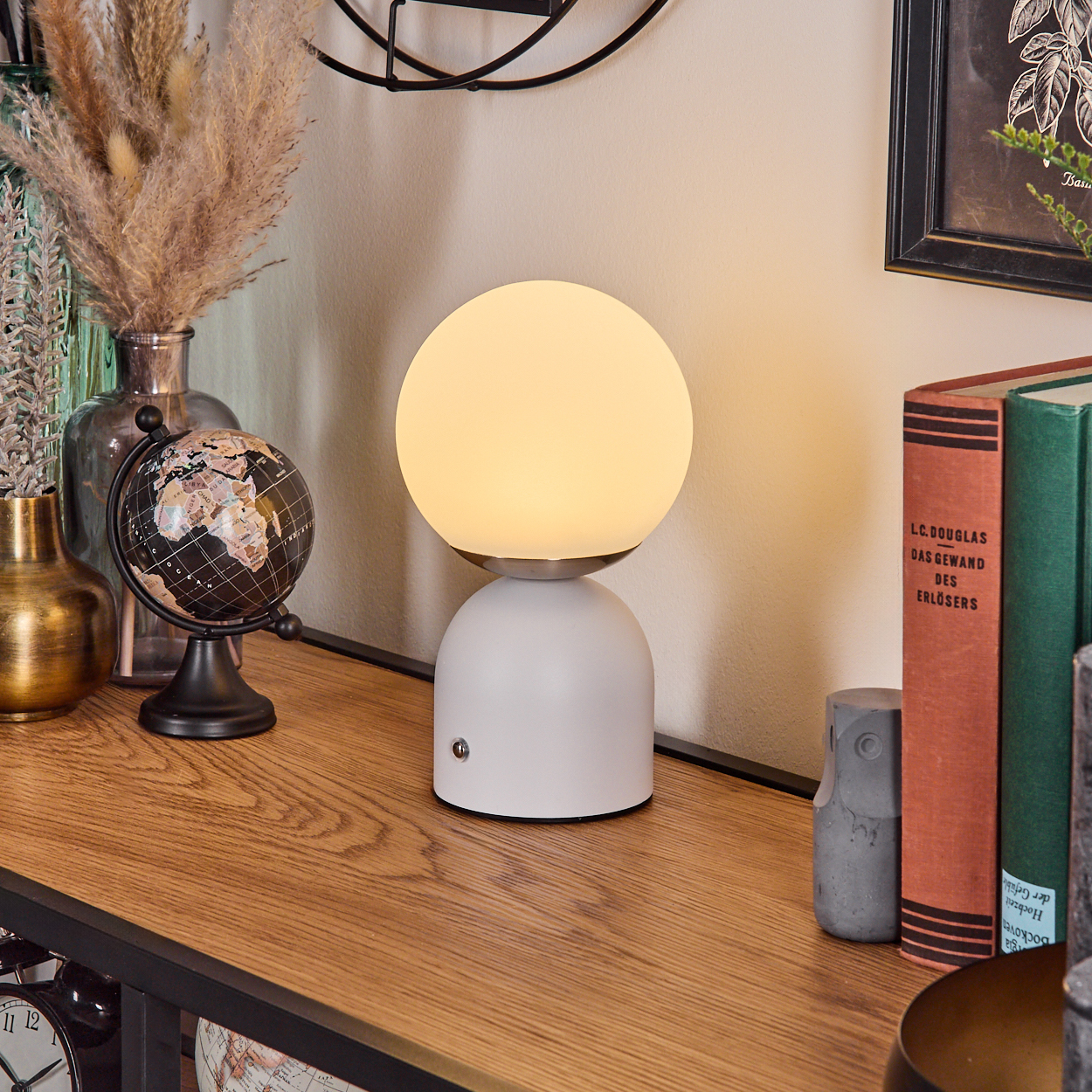 Eine weiße Lampe mit leuchtendem Globus steht auf einem Holzregal mit Büchern, einem Globus und anderen dekorativen Gegenständen.