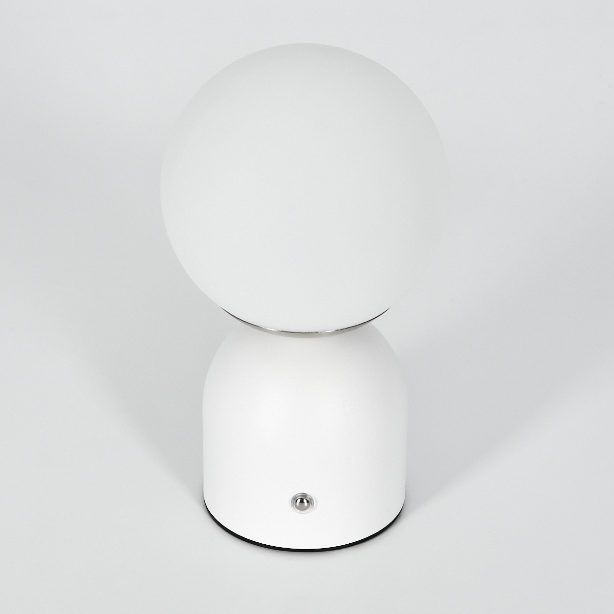 Eine weiße kugelförmige Lampe mit rundem Sockel. Die Lampe hat einen silbernen Ring zwischen Kugel und Sockel. Auf dem Sockel befindet sich ein Knopf.