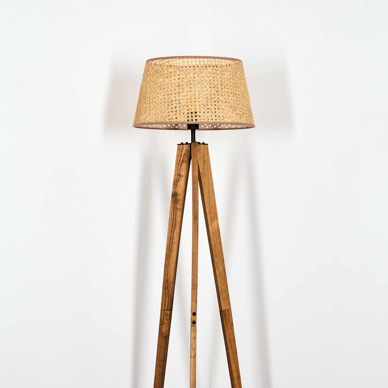 Eine Stehlampe mit Holzstativ und gewebtem Lampenschirm vor einer weißen Wand. Die Lampe besteht aus braunem Holz und der Schirm ist beige.