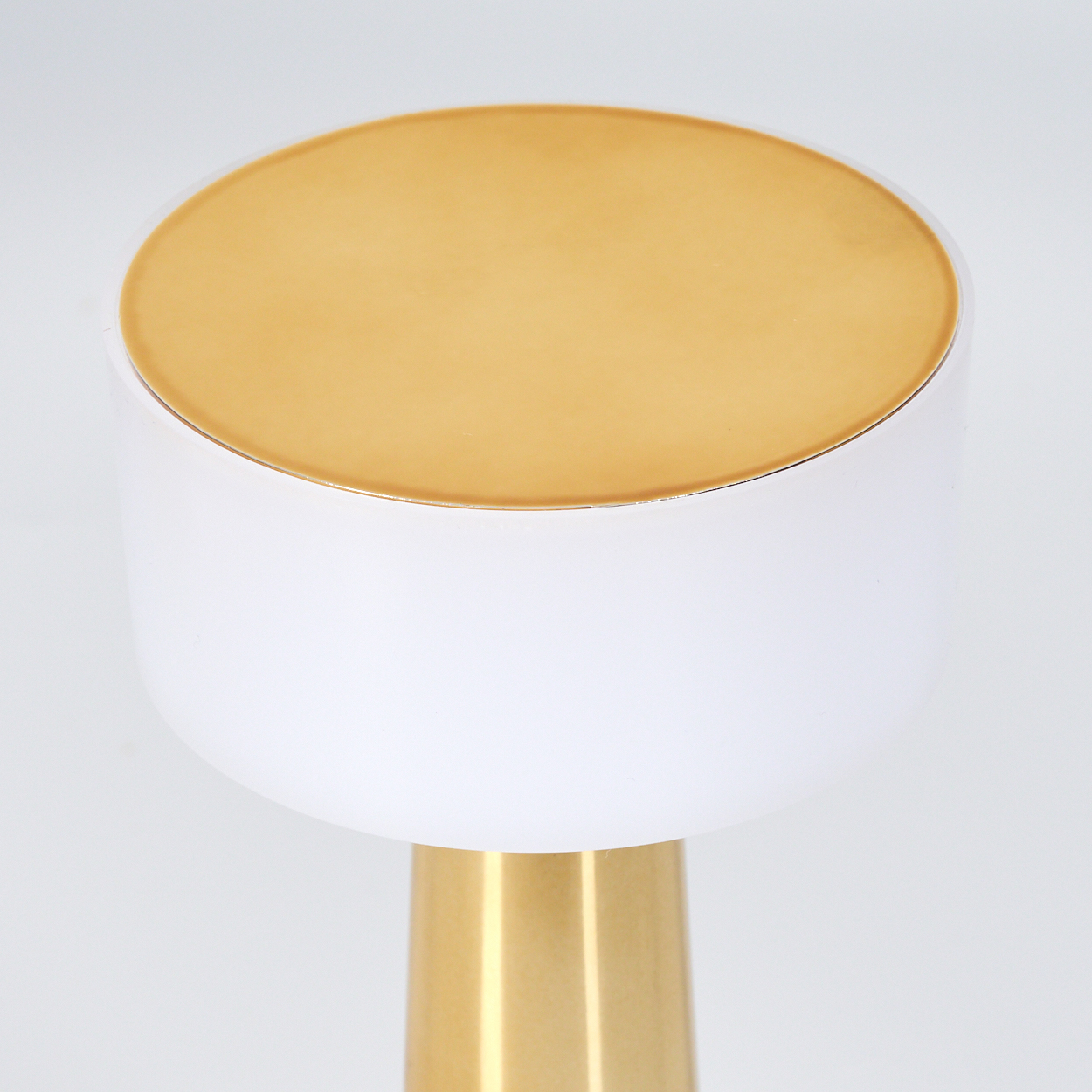 Eine moderne Lampe mit goldenem Oberteil, weißem Mittelteil und goldenem Sockel. Der Hintergrund ist schlicht weiß.