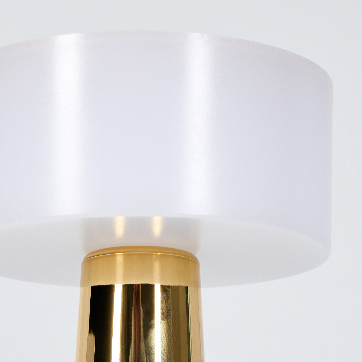 Nahaufnahme einer Lampe. Sie hat einen weißen Lampenschirm und einen goldenen Sockel. Der Hintergrund ist weiß.