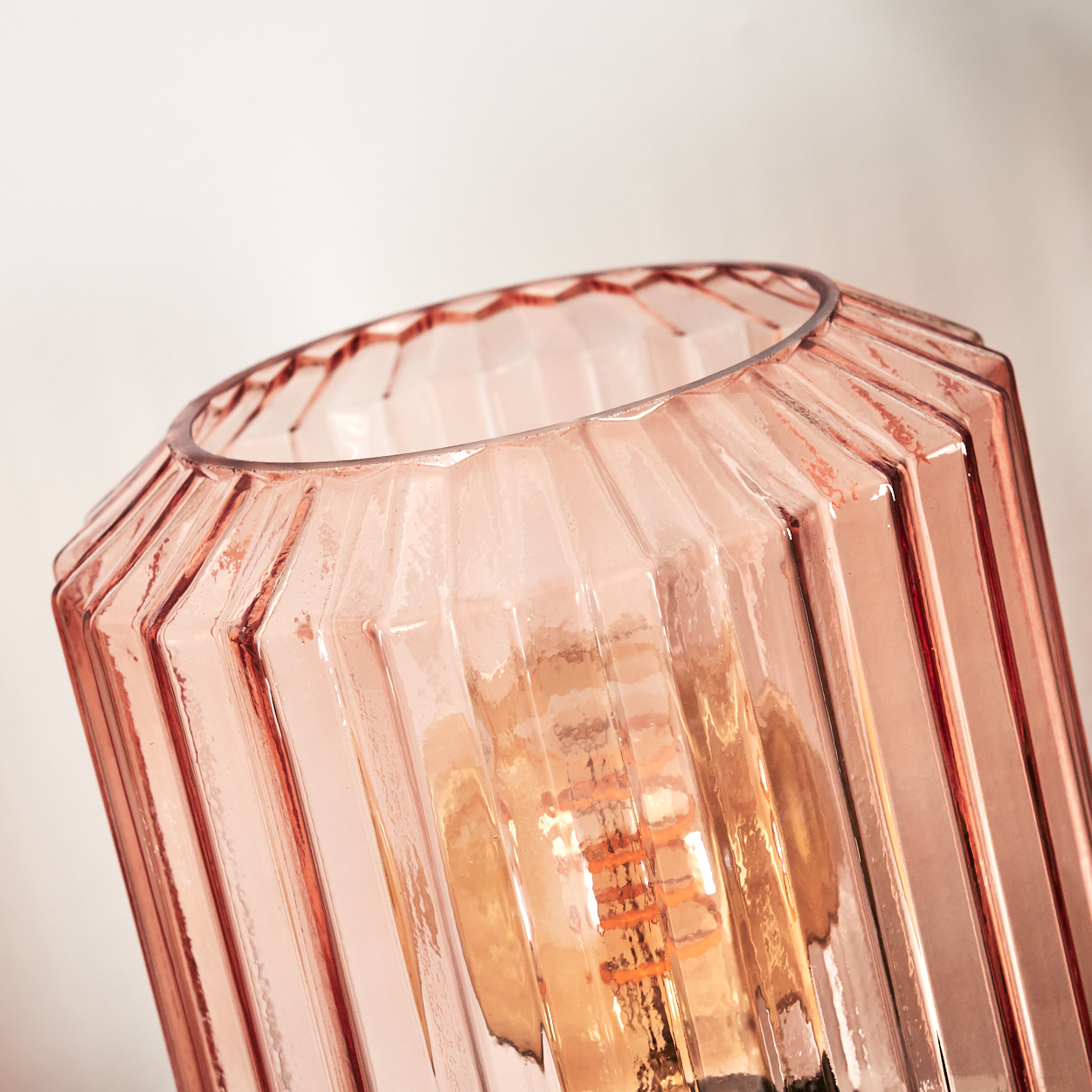 Nahaufnahme einer rosa Glaslampe. Sie hat ein geripptes Design mit einer freiliegenden Glühbirne im Inneren. Der Hintergrund ist weiß.