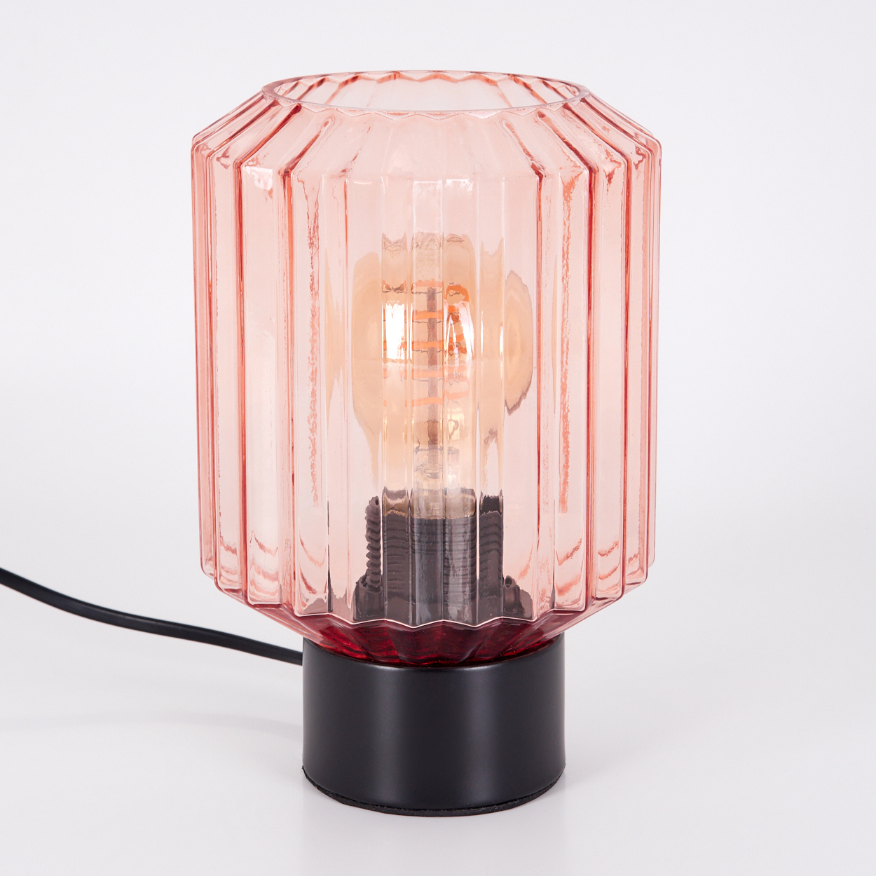 Eine rosa Glaslampe mit schwarzem Sockel und sichtbarer Glühbirne. Der Hintergrund ist weiß.