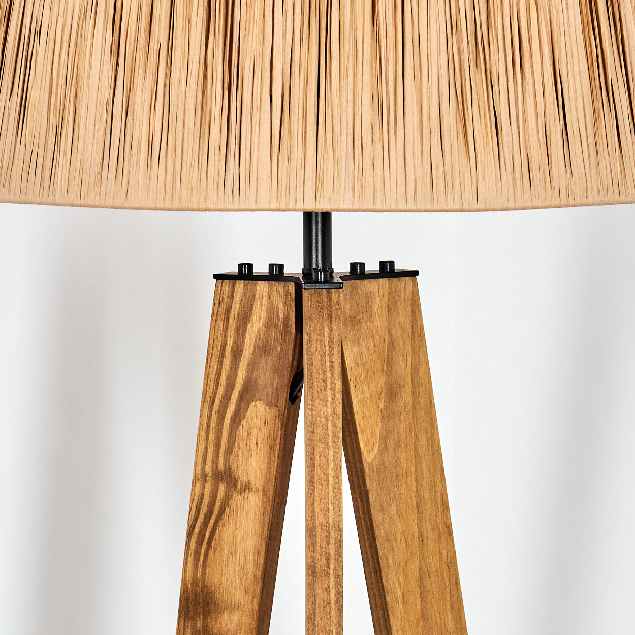 Eine Stehlampe mit hölzernem Dreibein und beigefarbenem Lampenschirm. Die Beine sind aus braunem Holz, verbunden mit schwarzem Metall. Weißer Hintergrund.