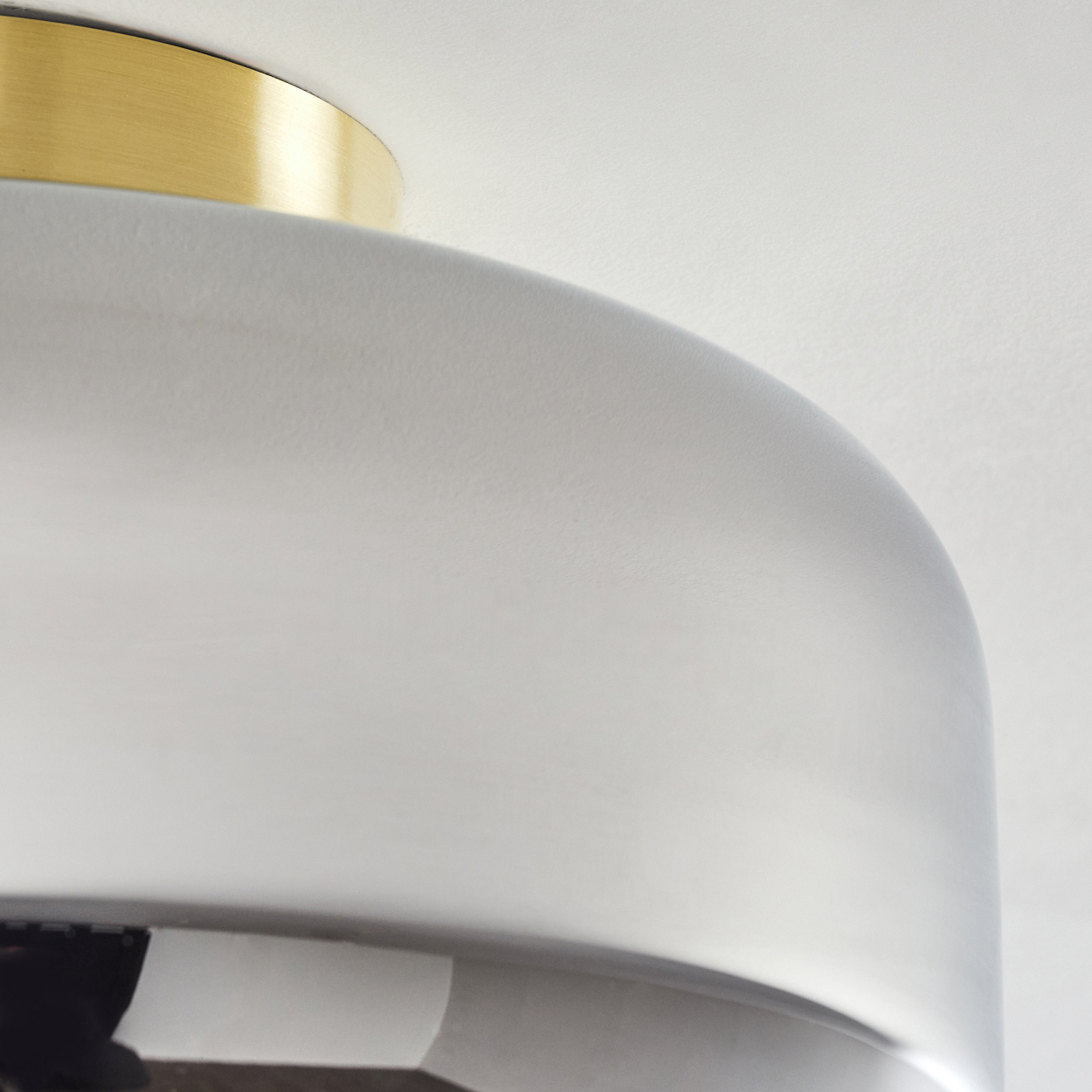 Nahaufnahme einer modernen Lampe. Die Lampe hat einen abgerundeten grauen Schirm mit goldfarbenem Oberteil, vor weißem Hintergrund.
