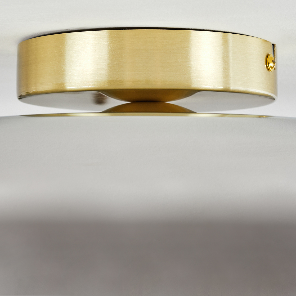 Nahaufnahme einer Deckenleuchte mit goldfarbenem Metallrand und weißer Oberfläche darunter.