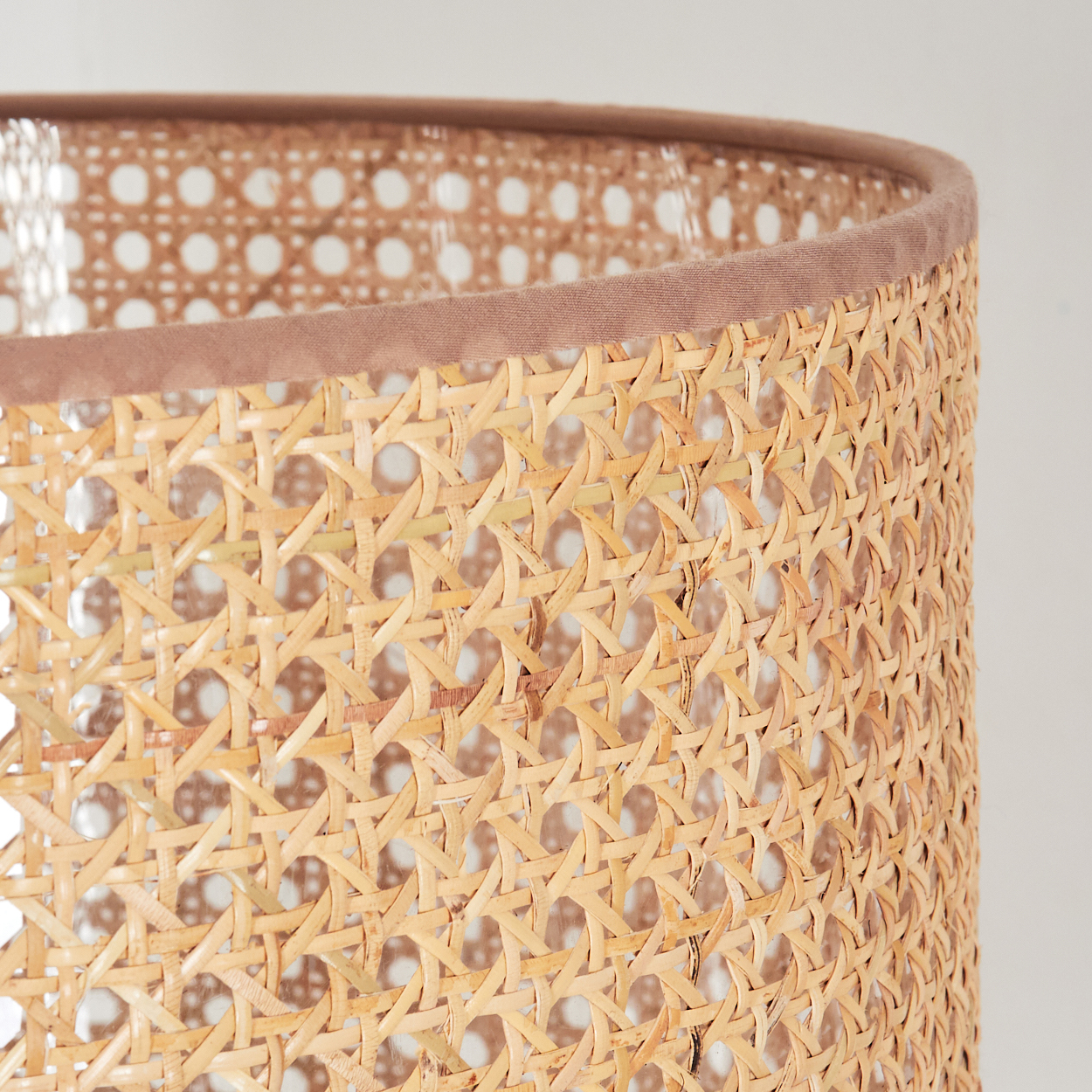 Nahaufnahme eines gewebten Lampenschirms aus Rattan. Der obere Rand ist mit einem braunen Stoff beschnitten. Der Hintergrund ist weiß.