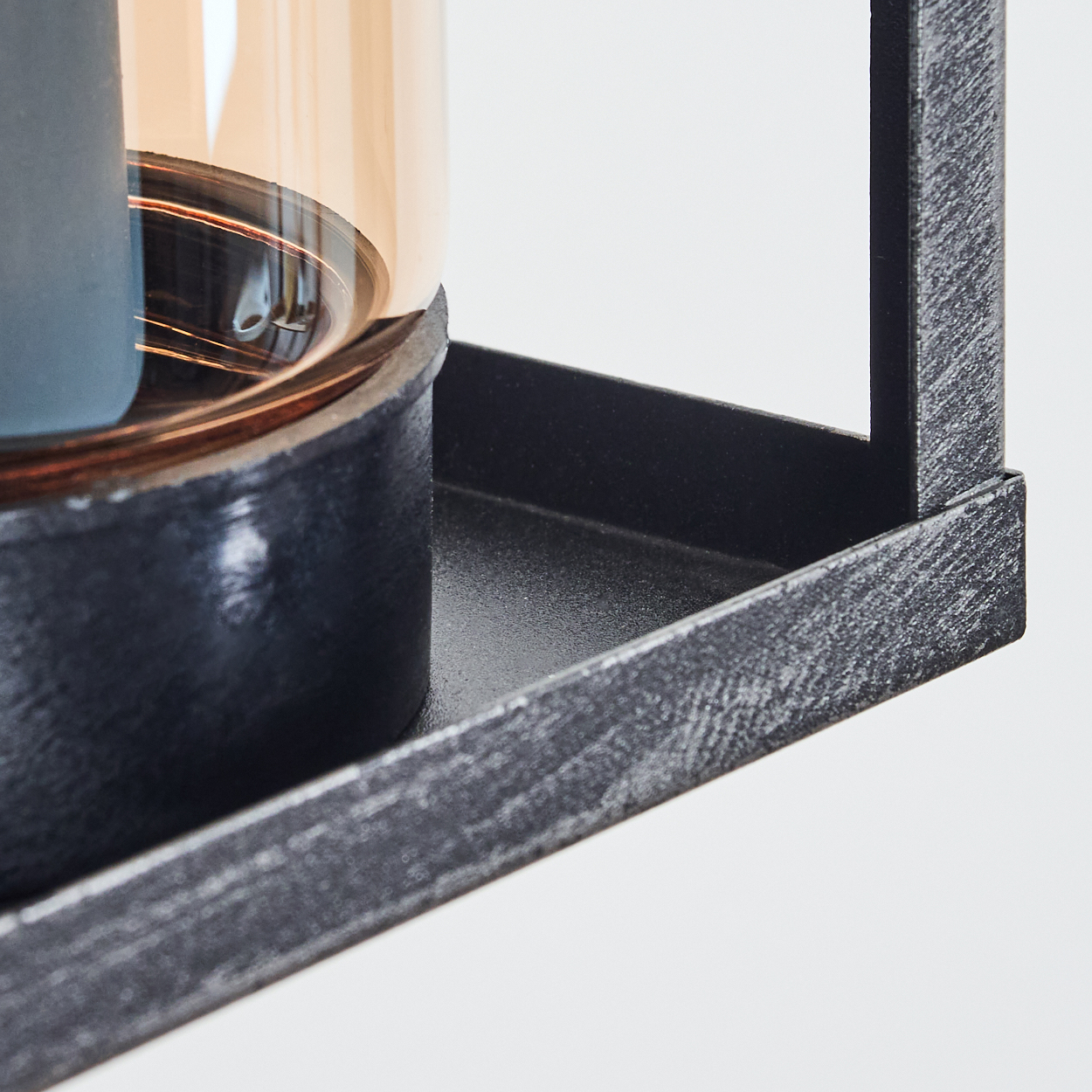 Nahaufnahme einer schwarzen Metalllaterne mit einer Kerze darin. Die Kerze befindet sich in einem braunen Glas. Weißer Hintergrund.