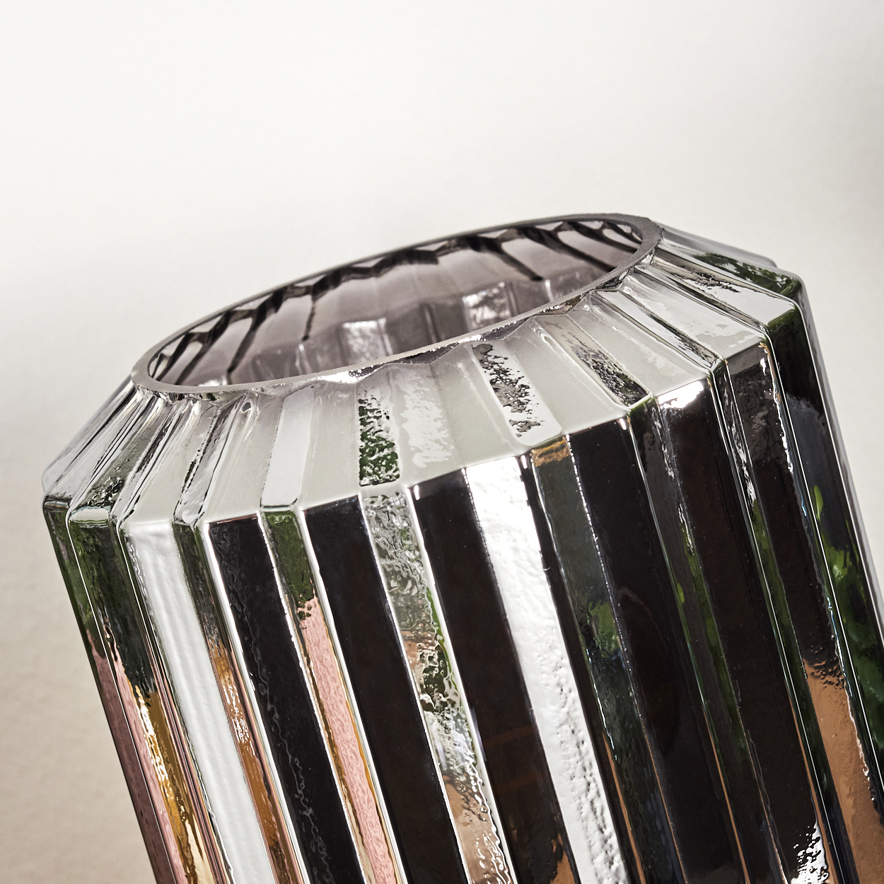 Nahaufnahme einer glänzenden, silbernen Vase mit vertikalen Rippen. Sie hat eine weite Öffnung und reflektiert Licht mit abwechselnden dunklen und hellen Streifen.