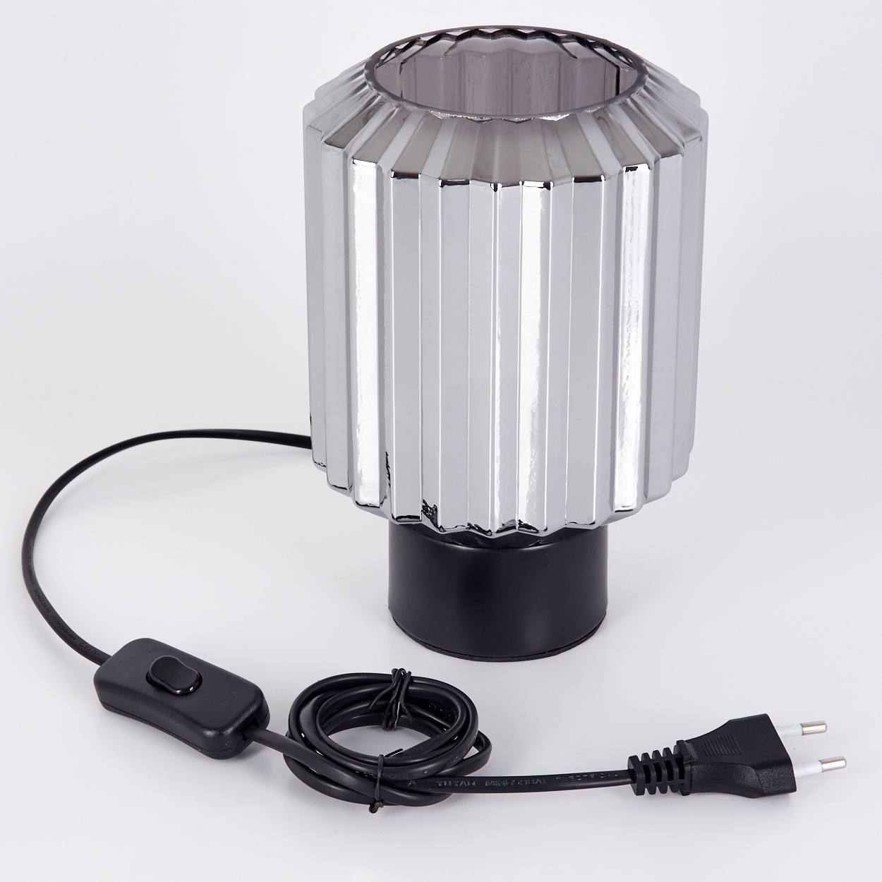 Eine silberne Lampe mit schwarzem Sockel und einem schwarzen Netzkabel mit Schalter. Die Lampe ist zylindrisch mit vertikalen Linien.