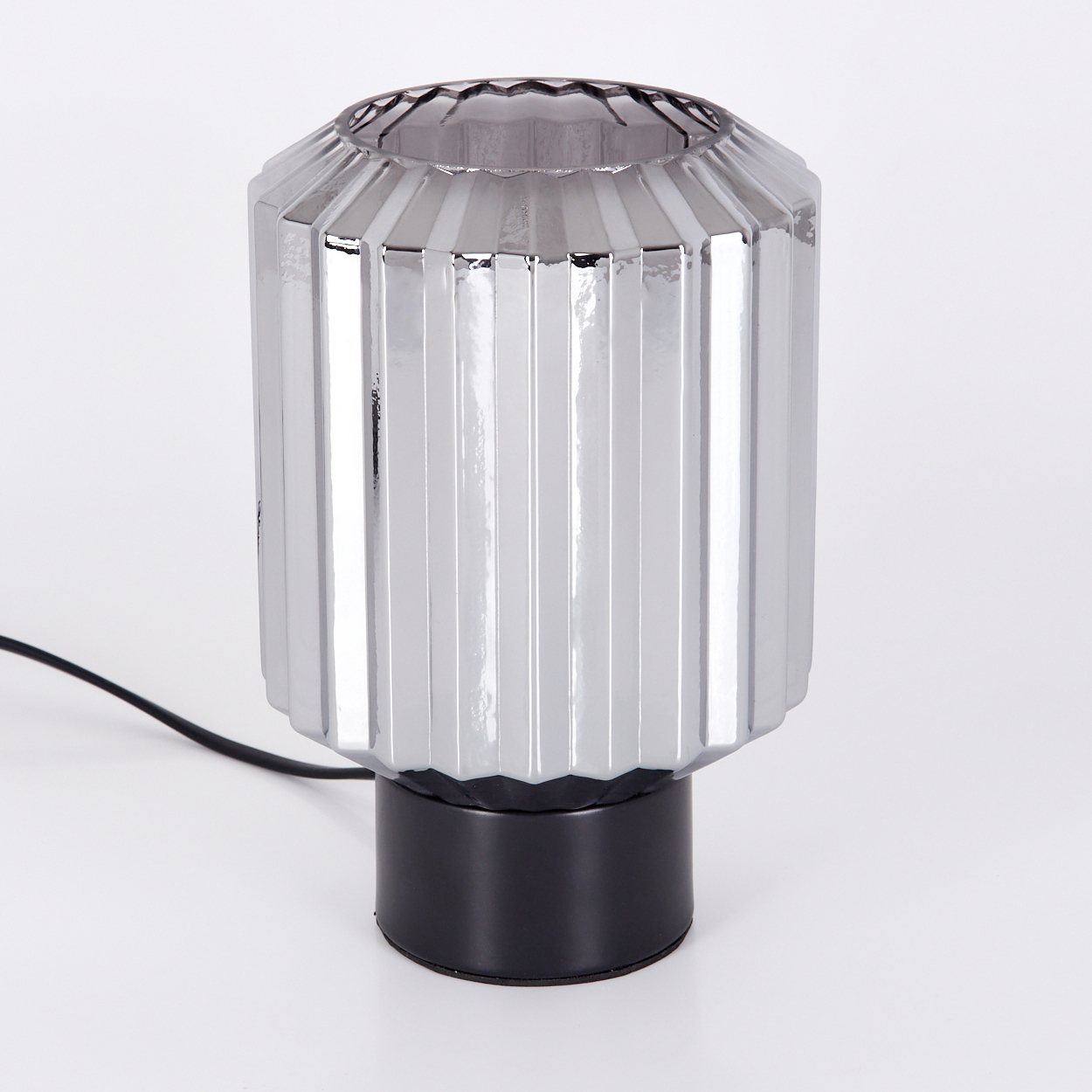 Eine graue, gerippte Glaslampe mit schwarzem Sockel steht auf einer weißen Oberfläche. Ein schwarzes Kabel geht von der Lampe aus. Der Hintergrund ist weiß.