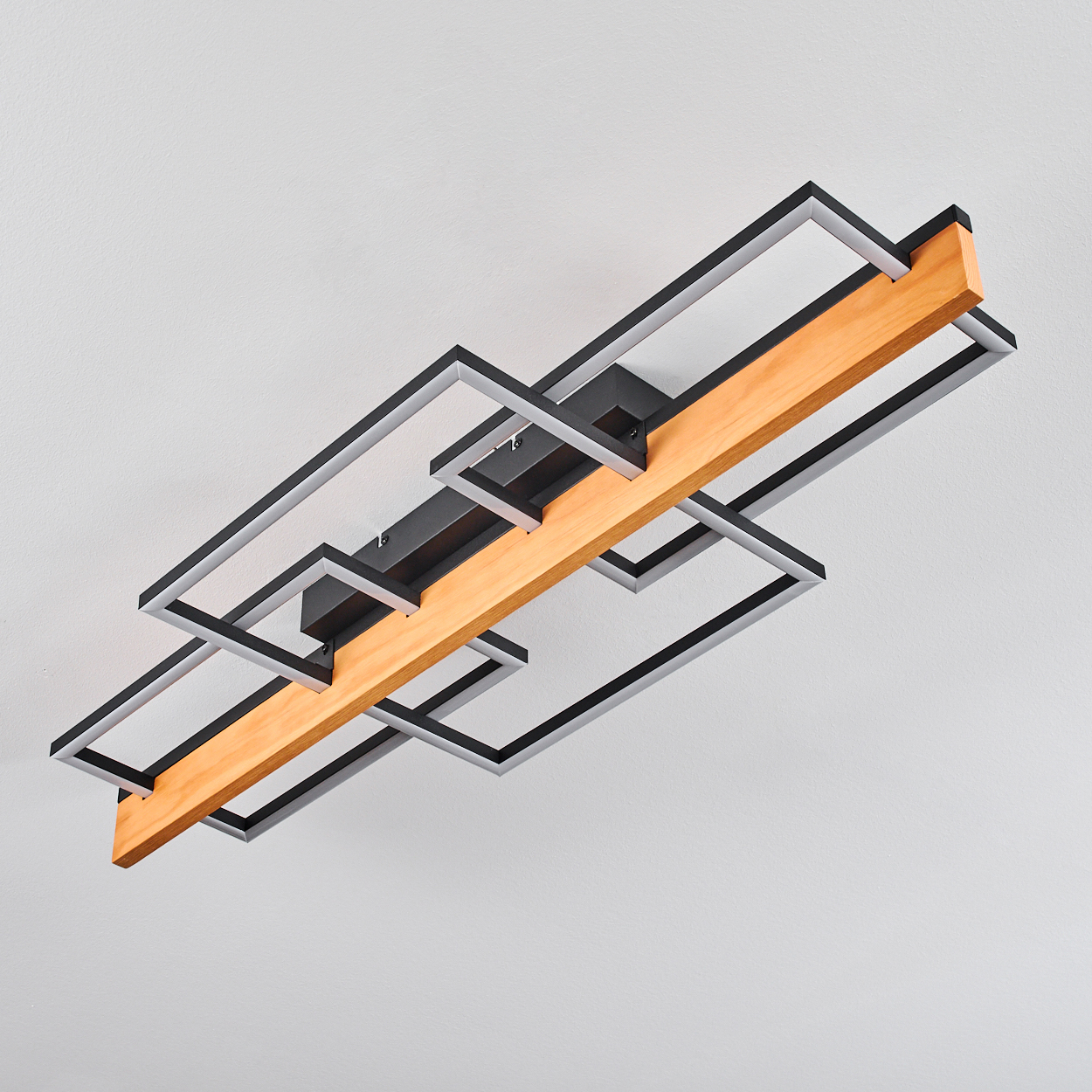 Eine moderne Deckenlampe mit Holzbalken und schwarz-silbernem Metallrahmen. Der Hintergrund ist eine schlichte weiße Decke.