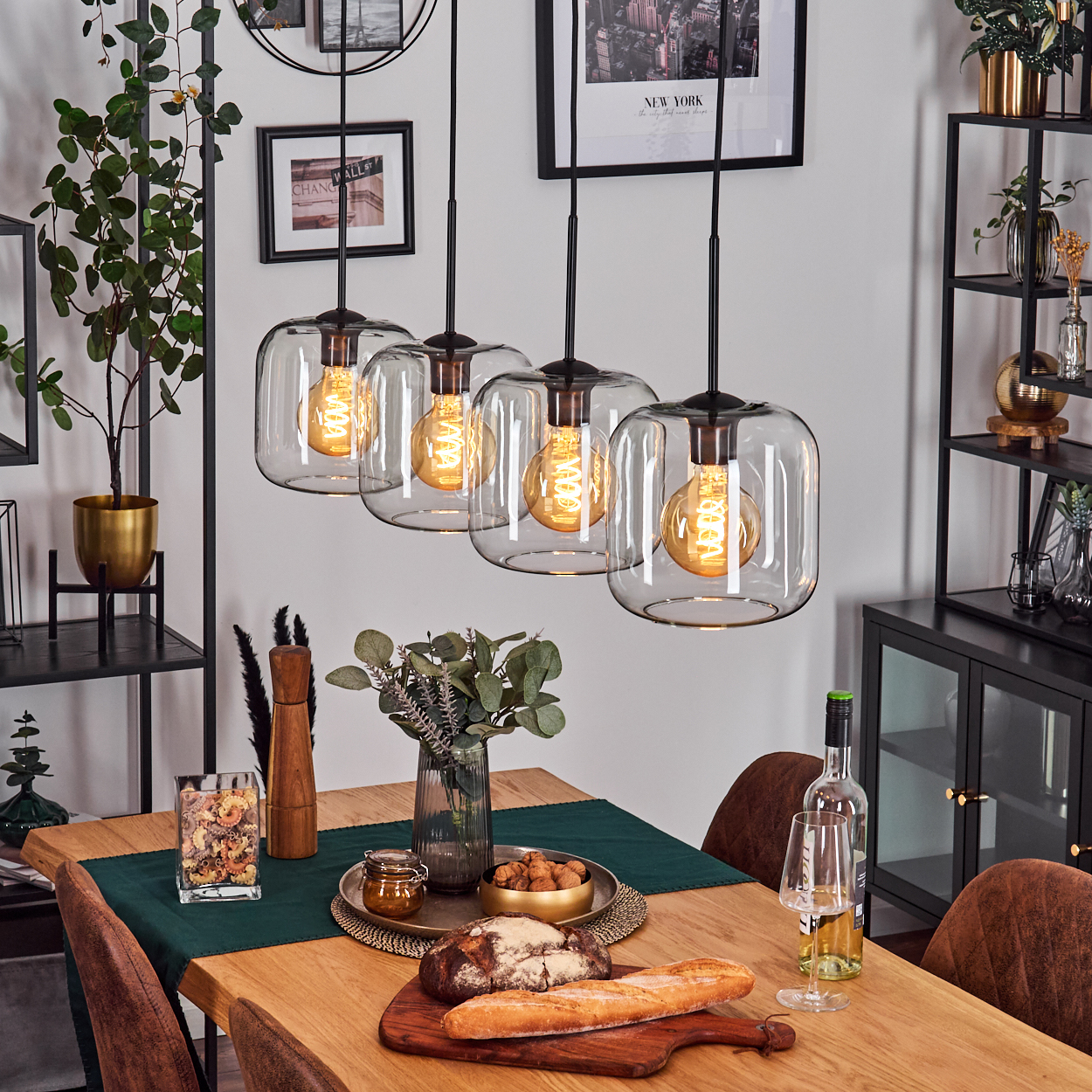 Ein Esszimmer mit Holztisch, Pendelleuchten und Tischdeko mit Brot, Wein und Dekoration.