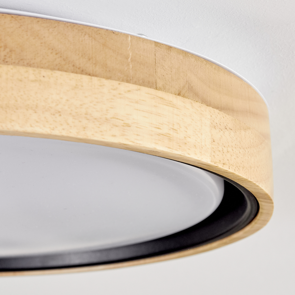 Nahaufnahme einer Deckenleuchte. Sie hat einen Holzrahmen, einen weißen Diffusor und eine schwarze Verkleidung. Der Hintergrund ist eine weiße Decke.