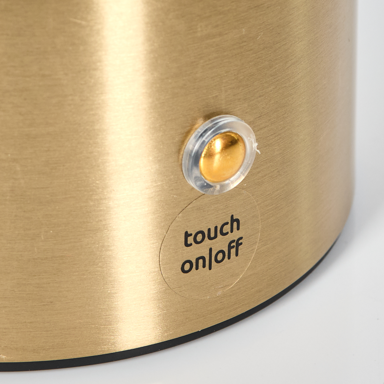 Ein goldfarbenes zylindrisches Objekt mit einer Touch-On/Off-Taste. Der Knopf ist rund und klar mit einem goldenen Zentrum.