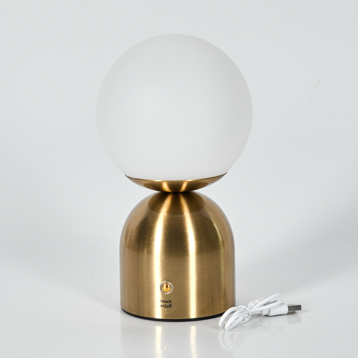 Eine goldene Tischlampe mit weißem kugelförmigen Schirm steht auf weißer Oberfläche. Ein USB-Kabel und eine „Touch on/off“-Taste sind sichtbar.