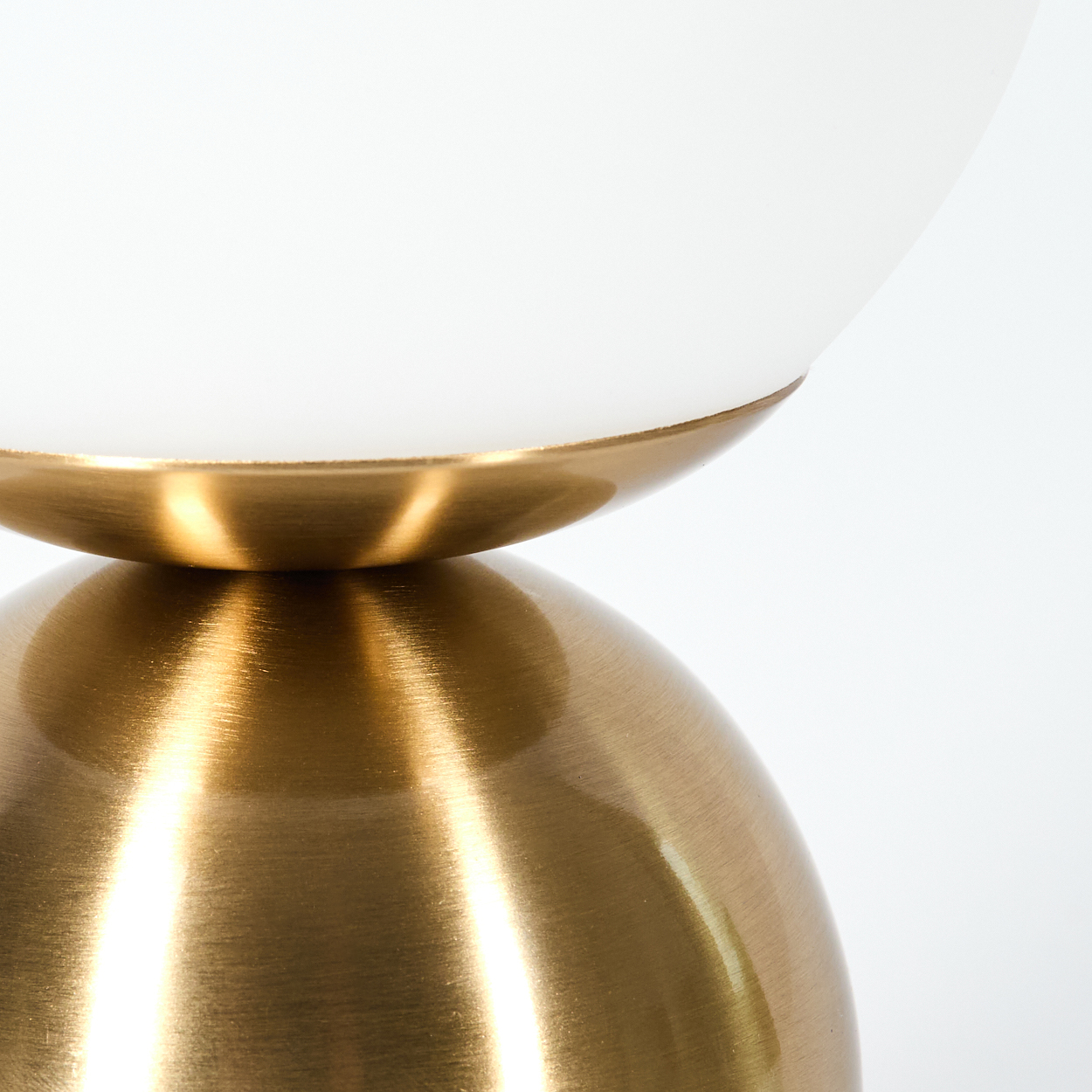 Nahaufnahme einer modernen Lampe. Sie hat einen goldenen Sockel und eine weiße, abgerundete Glaskuppel. Der Hintergrund ist weiß.