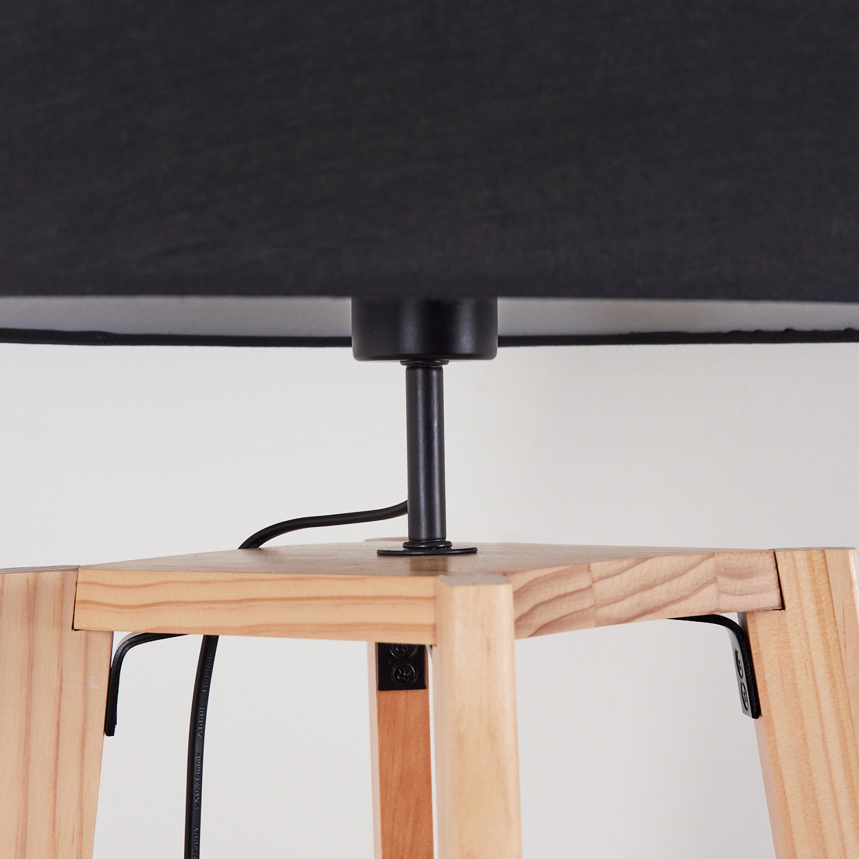 Nahaufnahme einer Lampe. Sie hat einen schwarzen Lampenschirm, einen schwarzen Stützpfosten und einen Holzsockel. Ein schwarzes Kabel ist ebenfalls sichtbar.