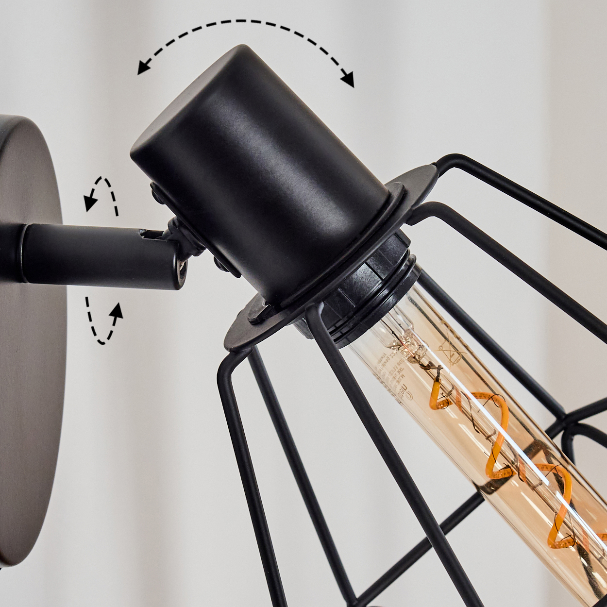 Schwarze Wandlampe mit käfigartigem Design. Die Lampe hat eine zylindrische Glühbirne mit Wendel. Pfeile zeigen die Einstellrichtung an.