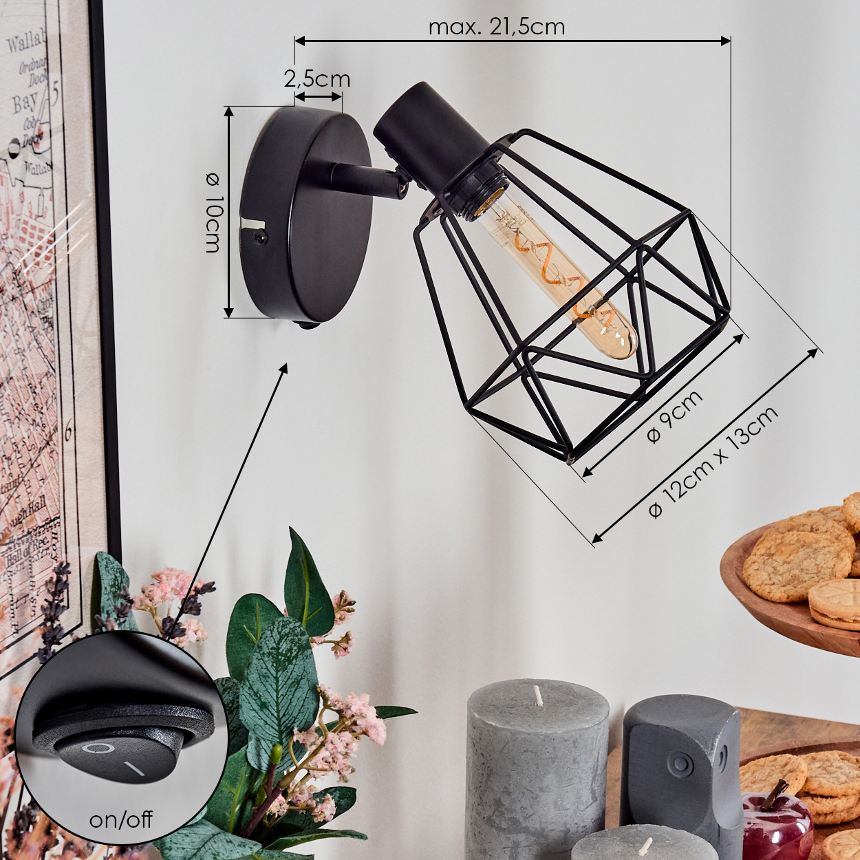 Eine schwarze Wandlampe mit geometrischem Käfigdesign, neben Blumen, Kerzen, Keksen und einer Karte.