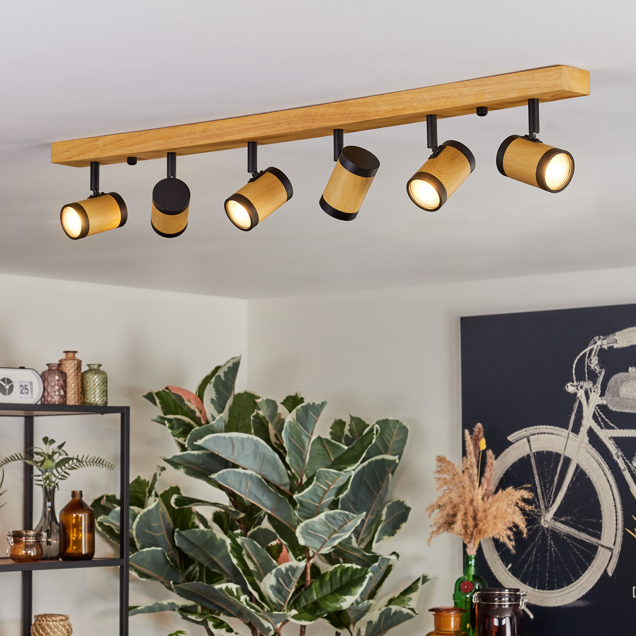 Deckenleuchten mit Holzbalken, schwarzen Strahlern, Pflanzen und einem Fahrradkunstwerk sind zu sehen.
