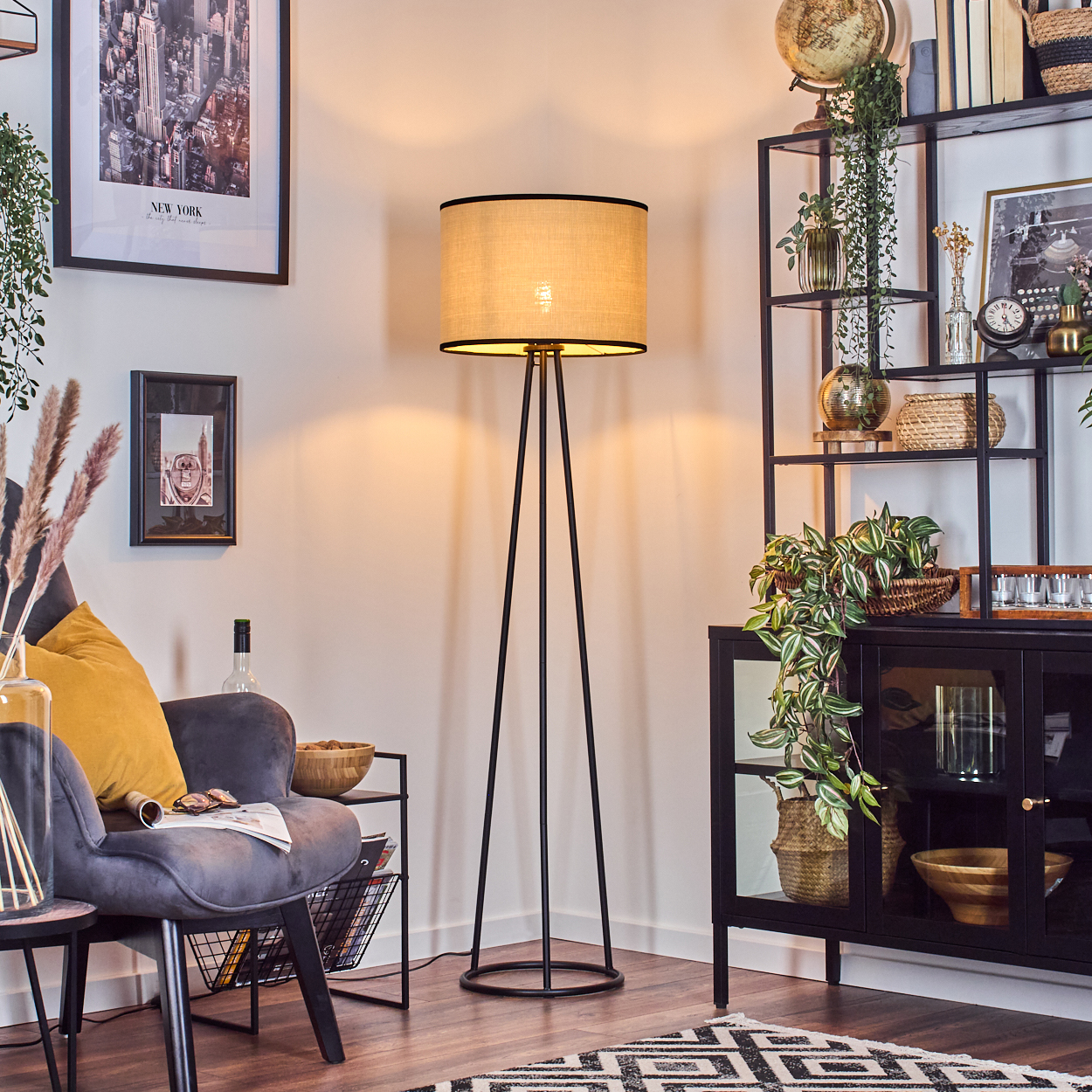 Ein Wohnzimmer mit Stehlampe, Sessel und schwarzem Regal mit Dekorationsartikeln. Auf dem Boden liegt ein Teppich.