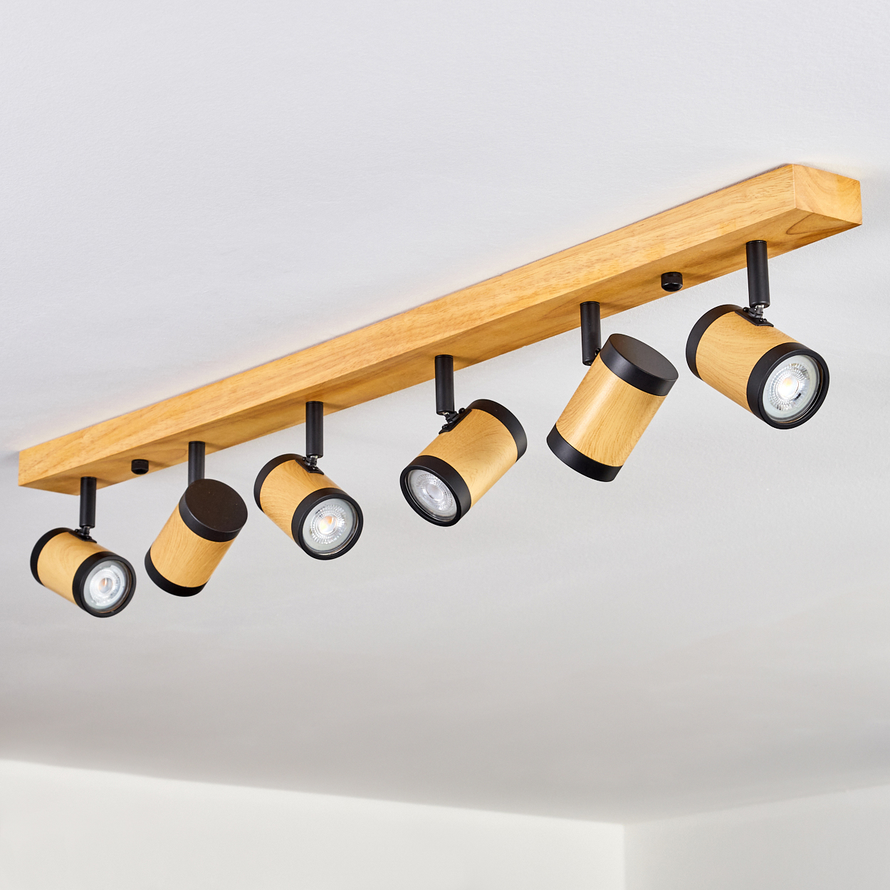 Eine Deckenleuchte aus Holzbalken mit sechs verstellbaren Strahlern. Die Strahler sind zylindrisch mit schwarzen und Holzoberflächen.