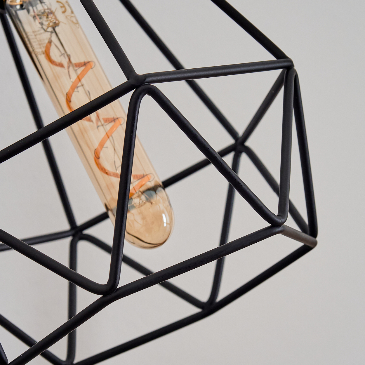 Nahaufnahme eines schwarzen geometrischen Lampenschirms mit einer Glühbirne. Der Hintergrund ist eine weiße Wand.