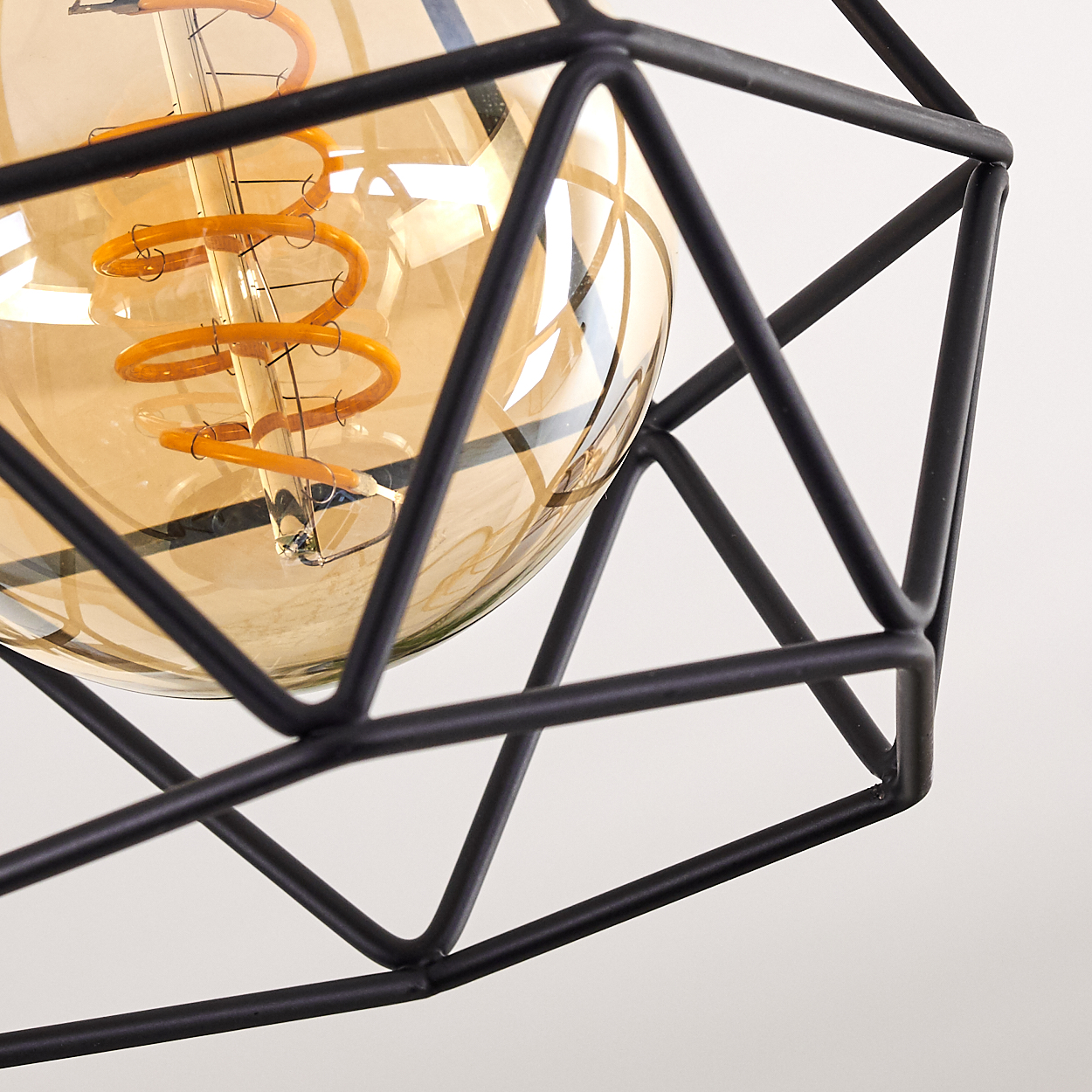 Nahaufnahme einer dekorativen Leuchte. Sie hat einen geometrischen schwarzen Metallrahmen um eine große, bernsteinfarbene Glühbirne mit Wendel.