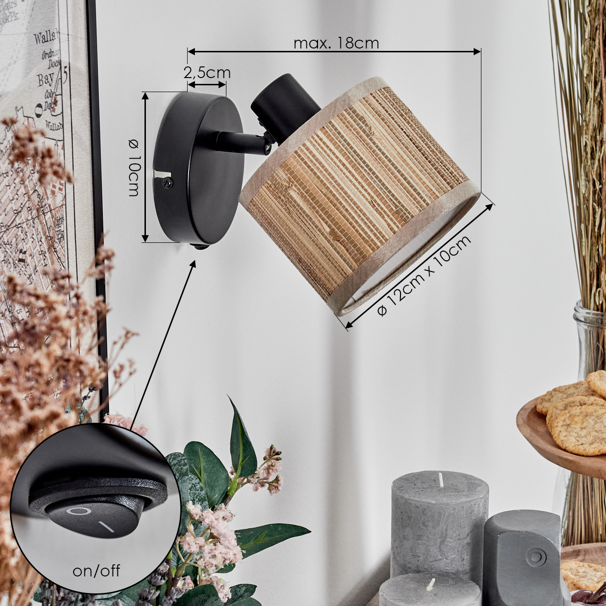 Eine schwarze Wandlampe mit beigem Lampenschirm. Die Lampe befindet sich neben einer Karte, Blumen, Kerzen und Keksen.
